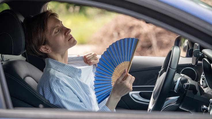 Mujer con calor usando un abanico dentro del carro porque no le funciona el aire acondicionado (Foto vía GettyImages)
