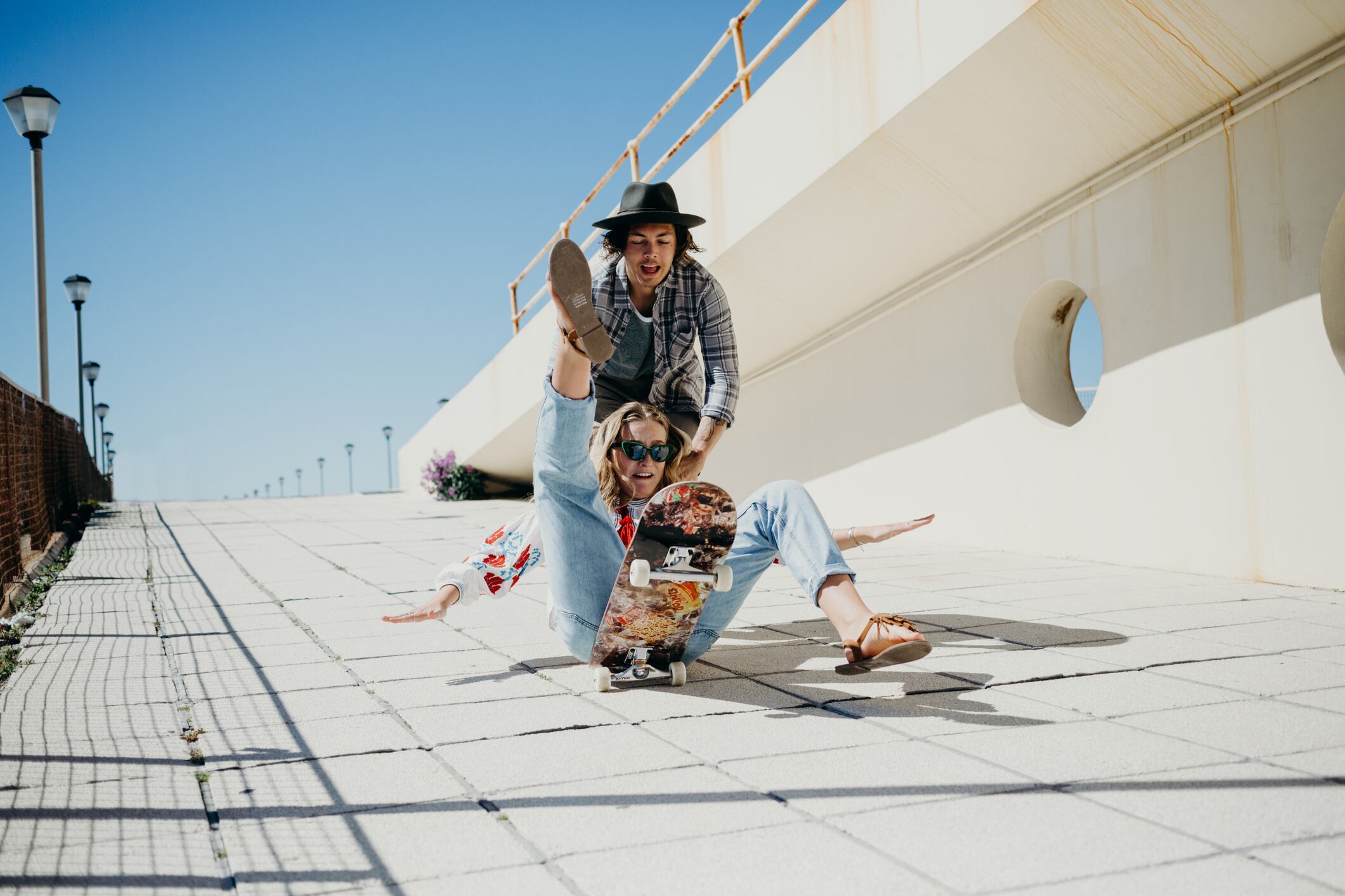 Young woman falling off skateboard while being pushed by young man