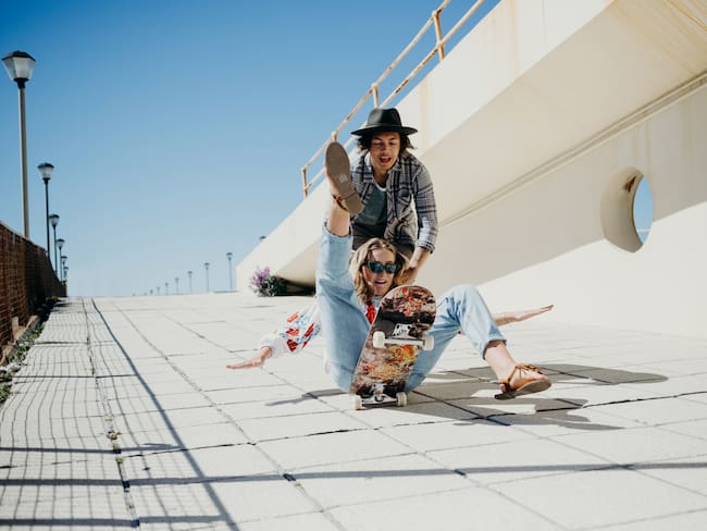 Young woman falling off skateboard while being pushed by young man