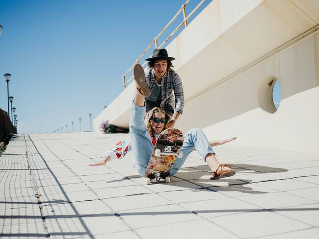 Young woman falling off skateboard while being pushed by young man