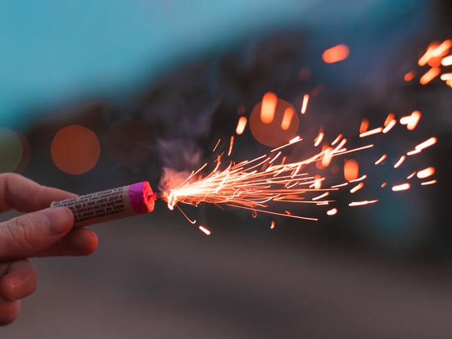 Young Man Lighting Up Firecracker in his Hand Outdoors in Evening. Guy Getting Ready for New Year Fun with Fireworks or Pyrotechnic Products - CloseUp Shot