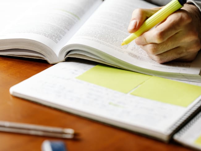 Crop anonymous male teacher with yellow marker pen reading book and making marks while preparing for lesson at table with notebook. Photo: Getty Images