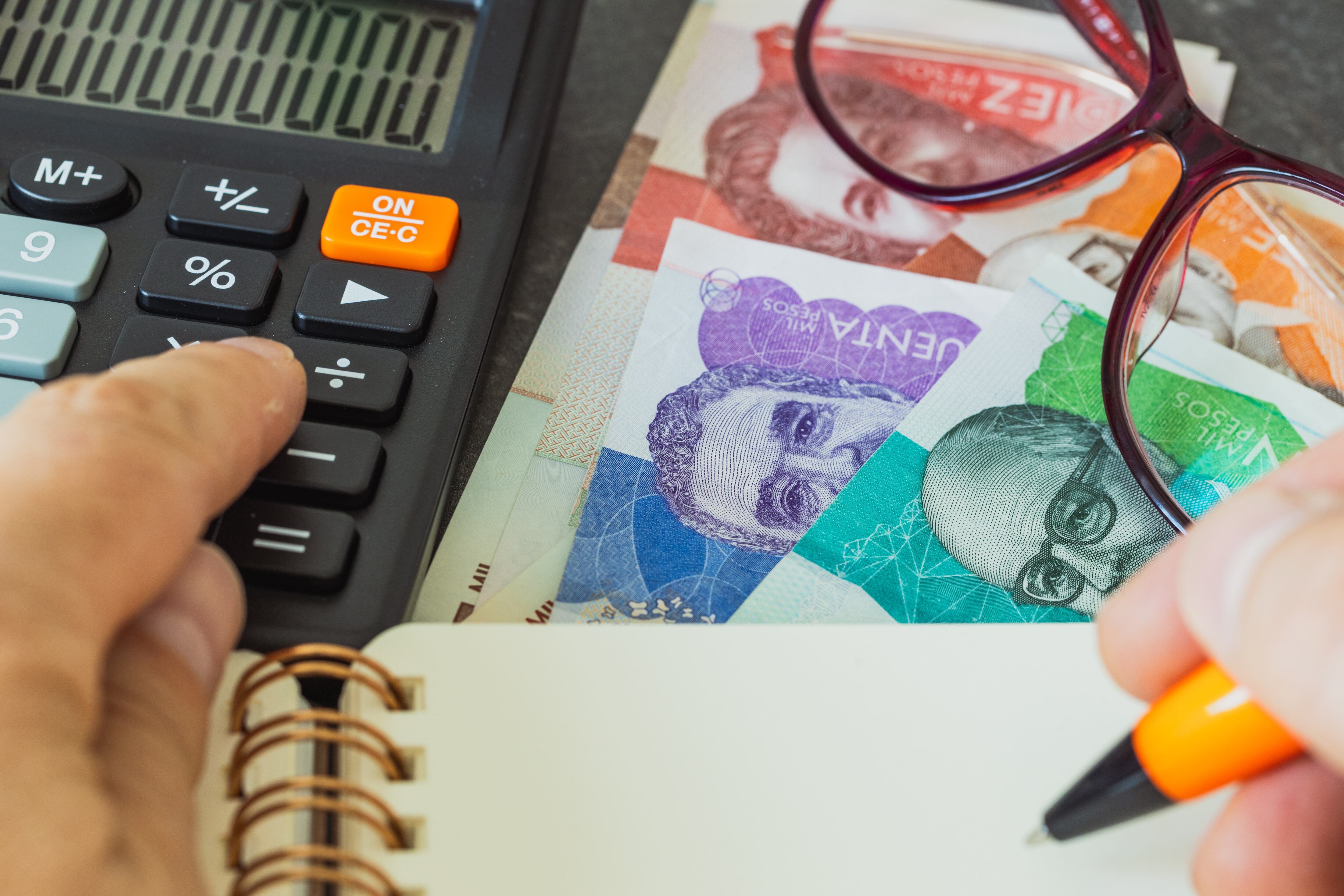 Persona usando una calculadora, al lado dinero colombiano (Foto: Getty Images)
