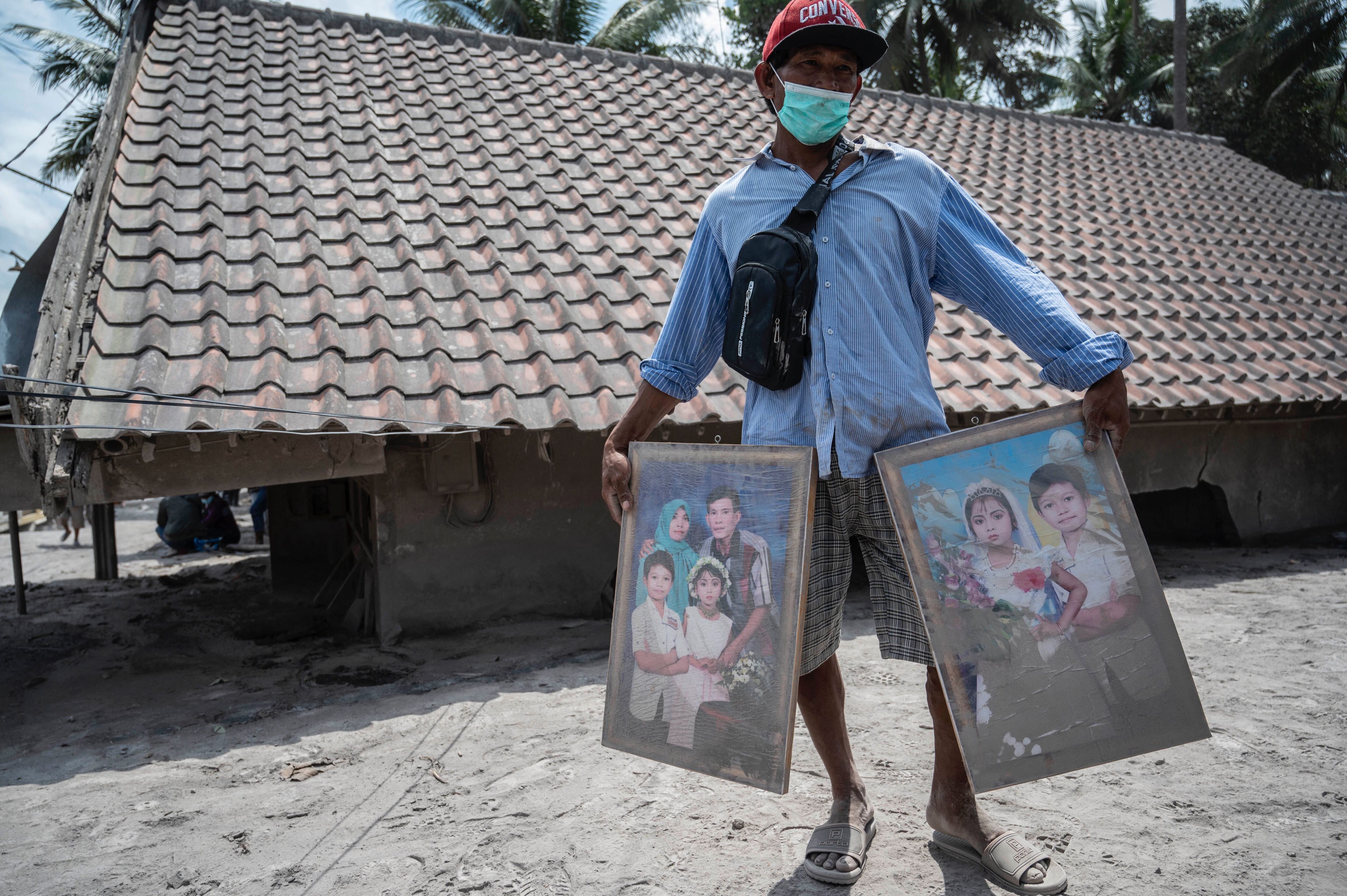 A villager cleans his family portraits he managed to salvage from his damaged home in Sumber Wuluh village in Lumajang on December 7, 2021, following the Mount Semeru eruption that killed at least 34 people. (Photo by Juni Kriswanto / AFP) (Photo by JUNI KRISWANTO/AFP via Getty Images)