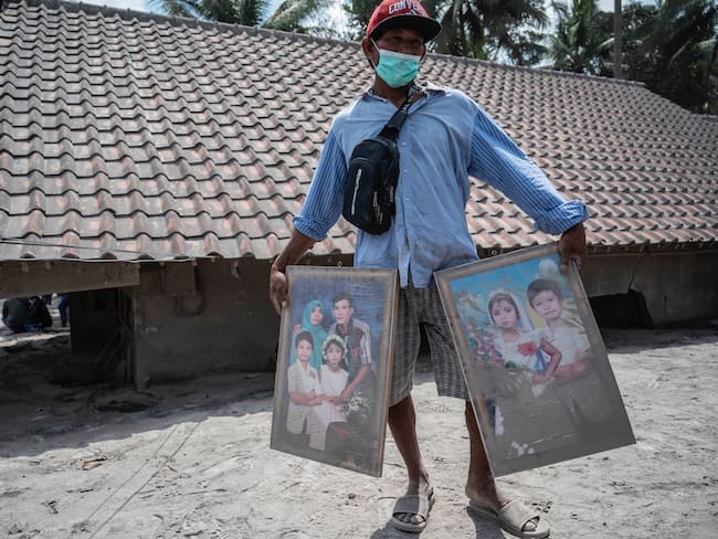 A villager cleans his family portraits he managed to salvage from his damaged home in Sumber Wuluh village in Lumajang on December 7, 2021, following the Mount Semeru eruption that killed at least 34 people. (Photo by Juni Kriswanto / AFP) (Photo by JUNI KRISWANTO/AFP via Getty Images)
