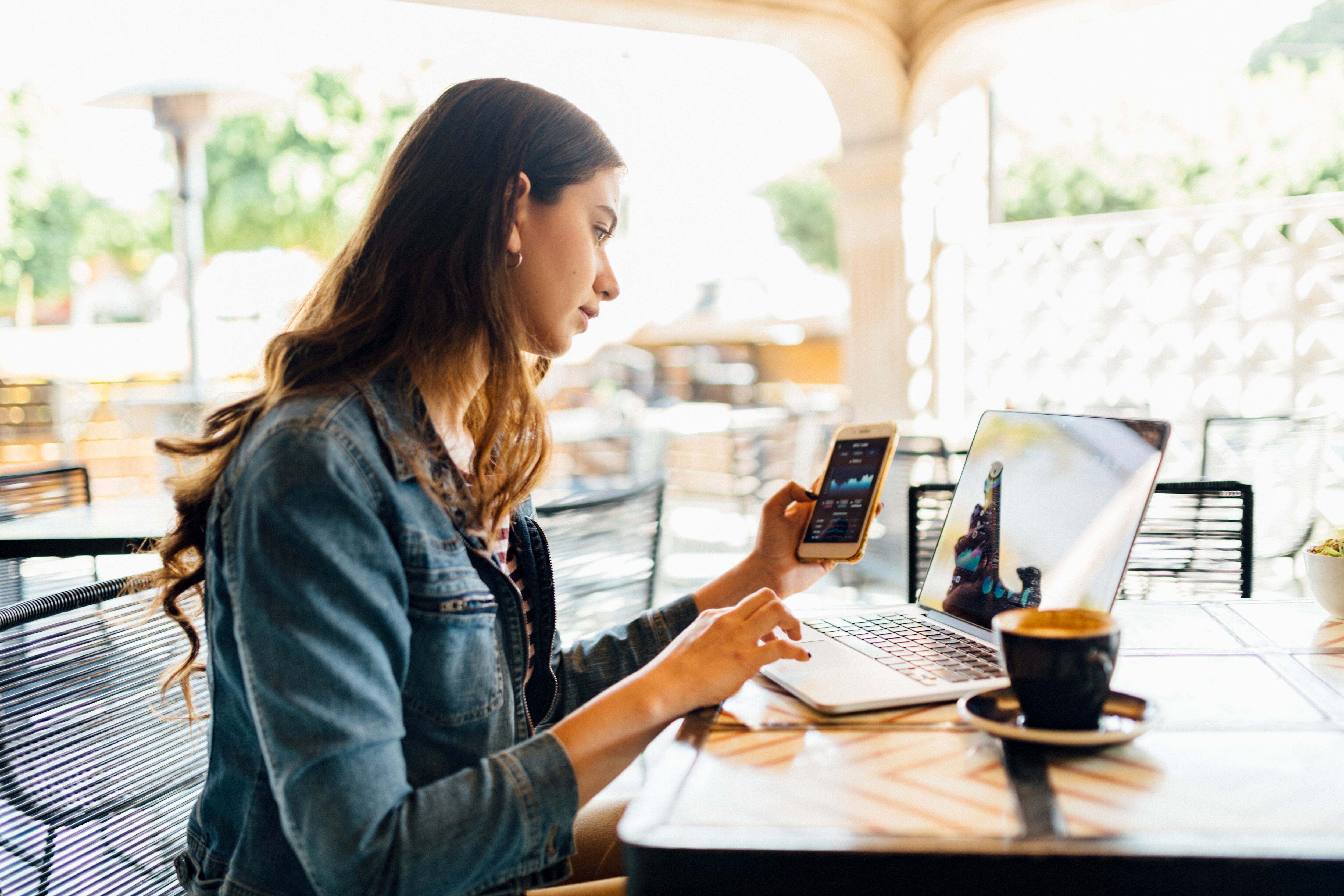Imagen de referencia de una mujer compartiendo datos móviles de su celular a un computador mientras está en un café / Foto: GettyImages