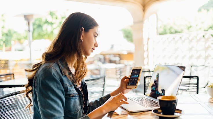 Imagen de referencia de una mujer compartiendo datos móviles de su celular a un computador mientras está en un café / Foto: GettyImages