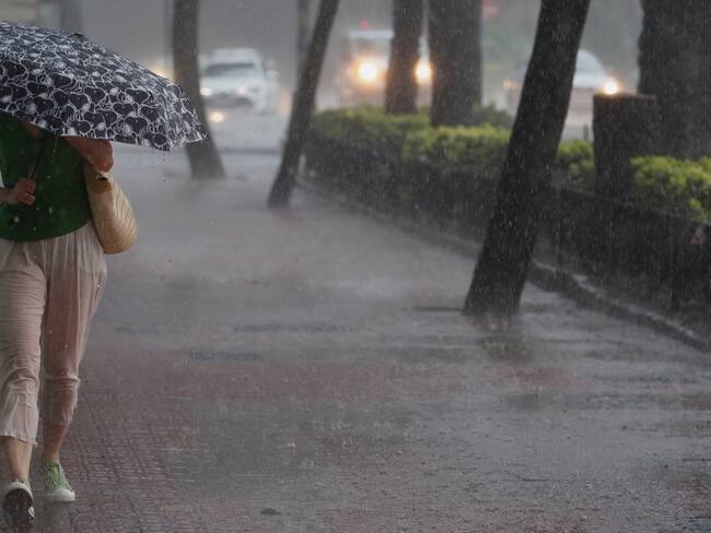 VALENCIA (ESPAÑA), 02/09/2023.- Una mujer camina por la acera bajo una intensa lluvia este sábado en Valencia. La Agencia Estatal de Meteorología (Aemet) ha activado para este sábado el riesgo naranja por lluvias de hasta 40 litros por metro cuadrado en una hora y tormentas que pueden ir acompañadas de granizo y rachas de viento muy fuerte en la provincia de Castellón y en el litoral de la de València. EFE/ Juan Carlos Cárdenas