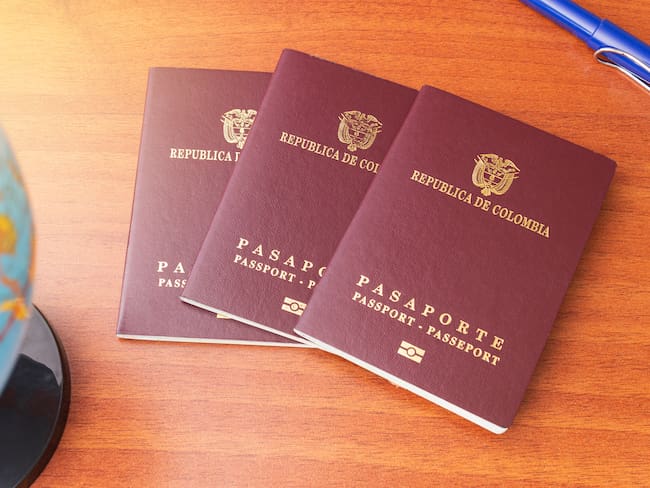 Tres pasaportes colombianos desplegados junto a un globo terráqueo y un bolígrafo en un escritorio de madera (Getty Images)