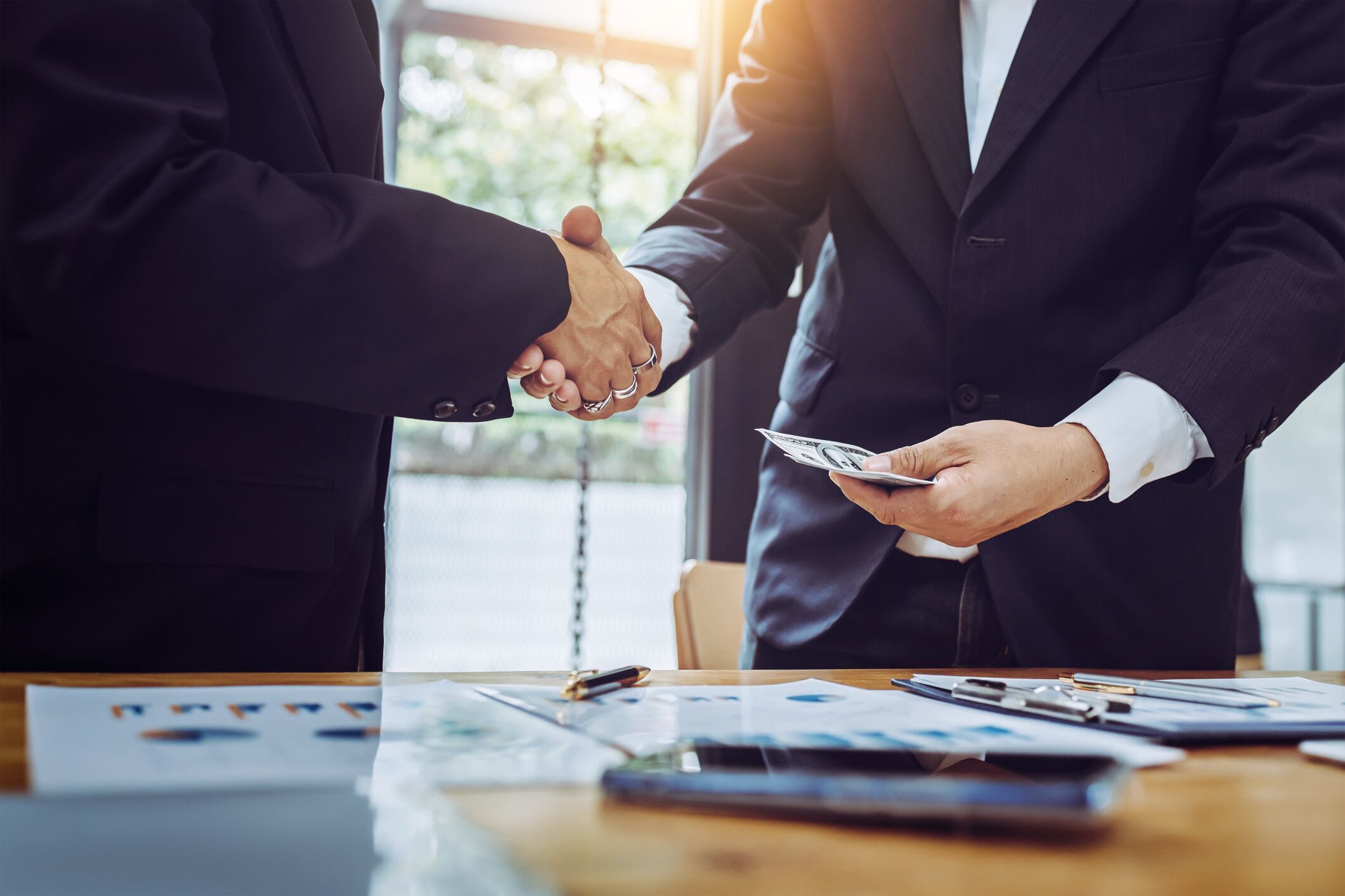 Shaking hands working together two business man while pay banknote in modern office.