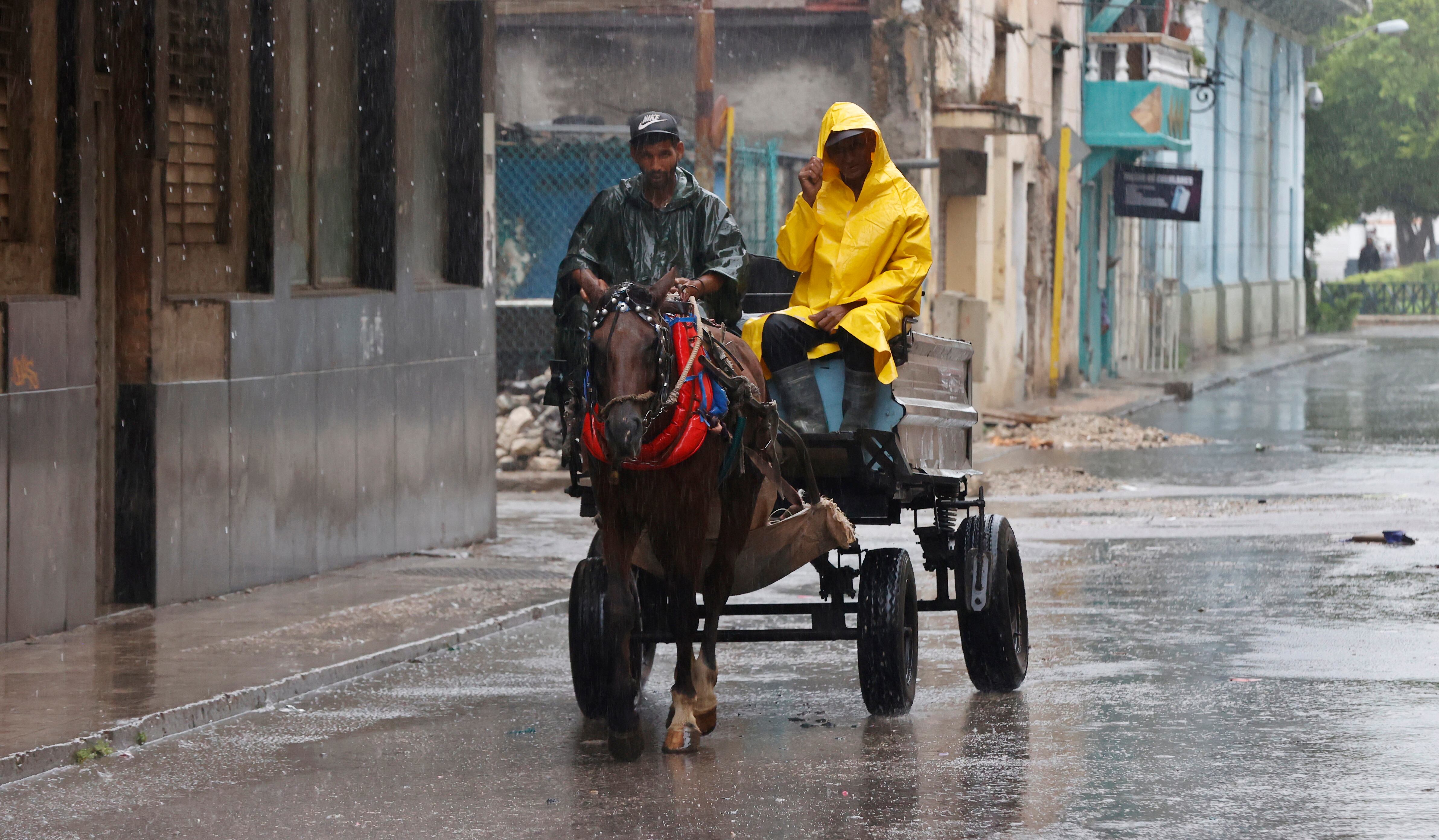 Dos hombres se transportan bajo la lluvia en un coche alado por un caballo. Foto: EFE.