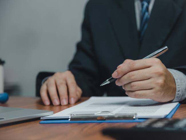 Hombre sosteniendo un bolígrafo con un informe sobre la mesa (Getty Images)
