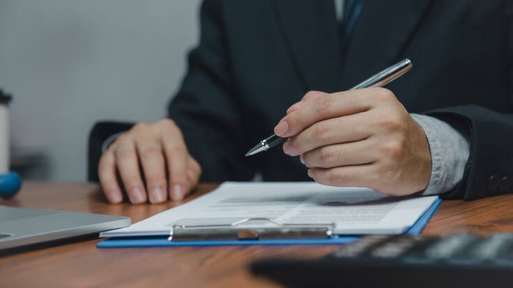 Hombre sosteniendo un bolígrafo con un informe sobre la mesa (Getty Images)