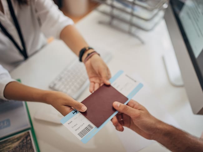 Two people, man in modern travel agency talking with woman who is working there, she is giving him a airplane ticket.
