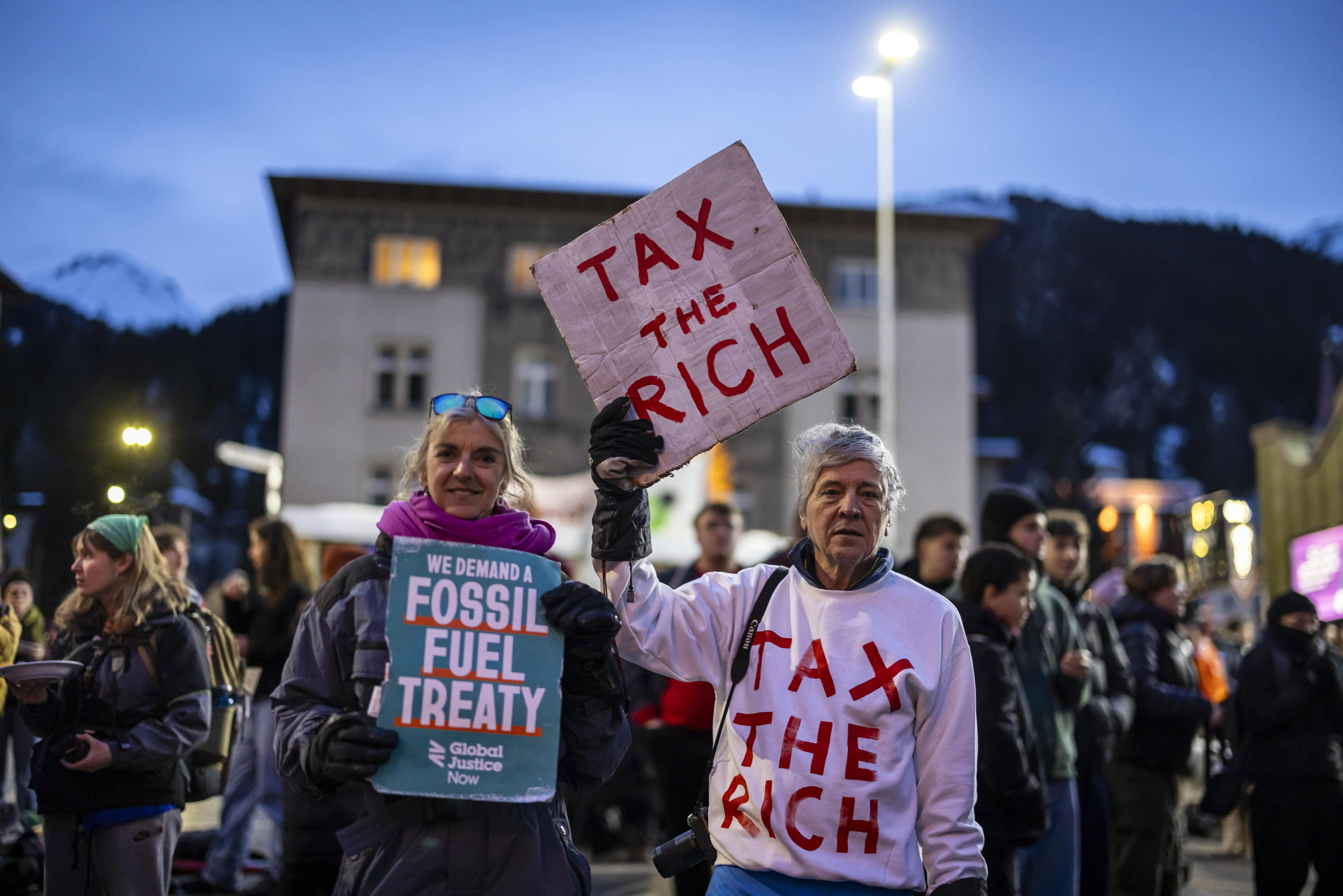 Davos (Suiza), 19/01/2025.- Phil White, de Patriotic Millionaires (dcha.), sostiene una pancarta en la que se lee «Impuestos a los ricos» mientras asiste a una manifestación antes de la reunión anual del Foro Económico Mundial.
