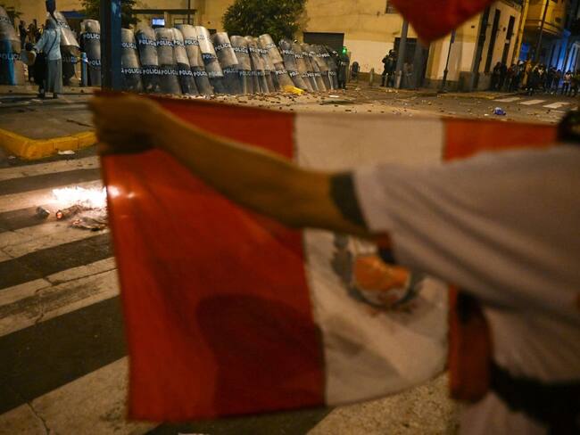 A demonstrator holds a Peruvian national flag in front of the riot police during a protest against the government of President Dina Boluarte in Lima on January 19, 2023. - Thousands of protesters began marching through Peru's capital Thursday to demand the president's resignation and fresh elections, following weeks of violent unrest that have left 44 people dead. (Photo by ERNESTO BENAVIDES / AFP) (Photo by ERNESTO BENAVIDES/AFP via Getty Images)