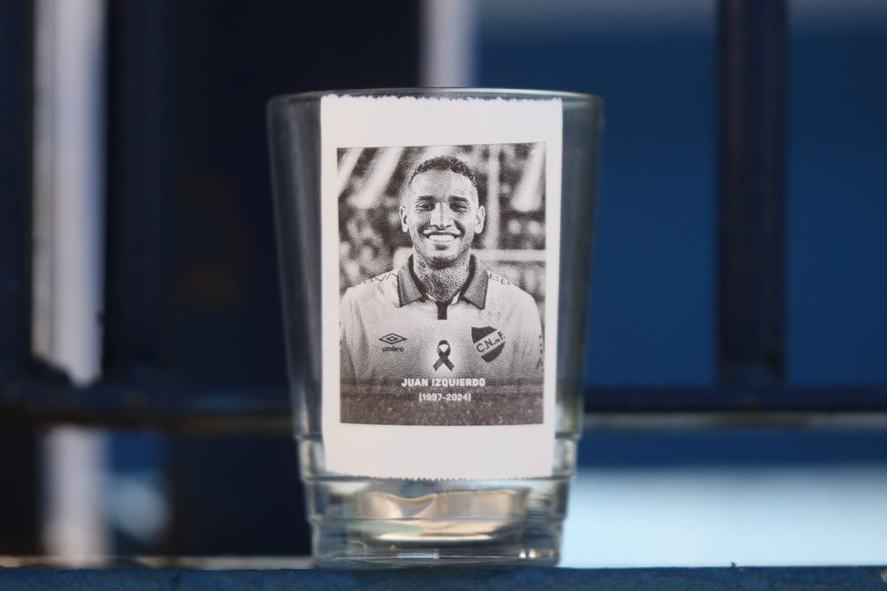 Fotografía que muestra una imagen del fallecido jugador Juan Izquierdo durante un homenaje este miércoles, en Montevideo (Uruguay). Fanáticos del uruguayo Nacional se acercaron hasta la sede del equipo para dejar flores y mensajes al futbolista Izquierdo, quien falleció un día antes en la ciudad brasileña de São Paulo. Debajo de una bandera del conjunto Tricolor que ondea a media asta, los hinchas dejaron camisetas con leyendas escritas de puño y letra. EFE/ Sofía Torres