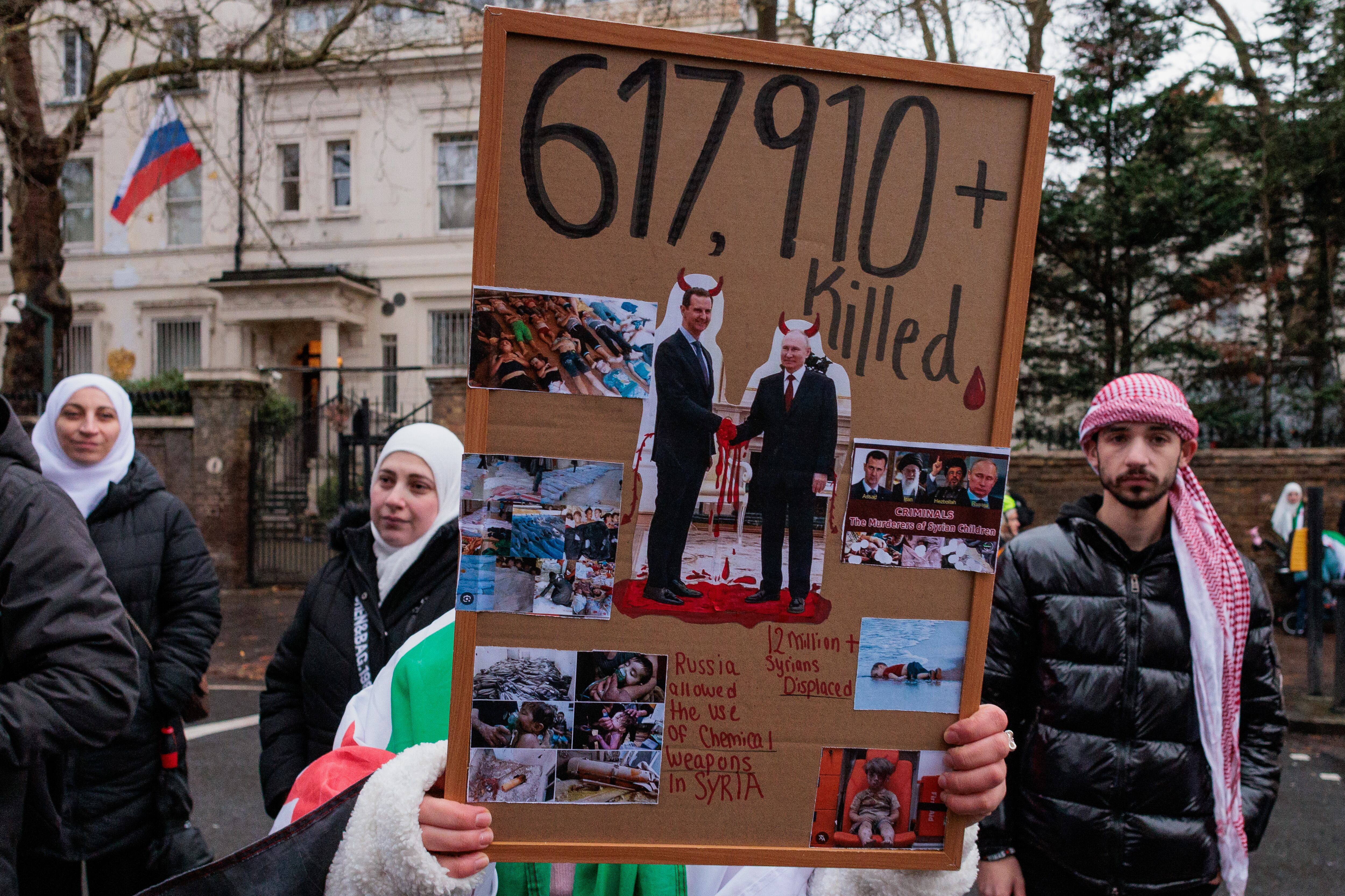 A Syria Solidarity Campaign activist holds a sign showing an image of Bashar al-Assad shaking hands with Vladimir Putin during a protest. (Mark Kerrison/In Pictures via Getty Images)