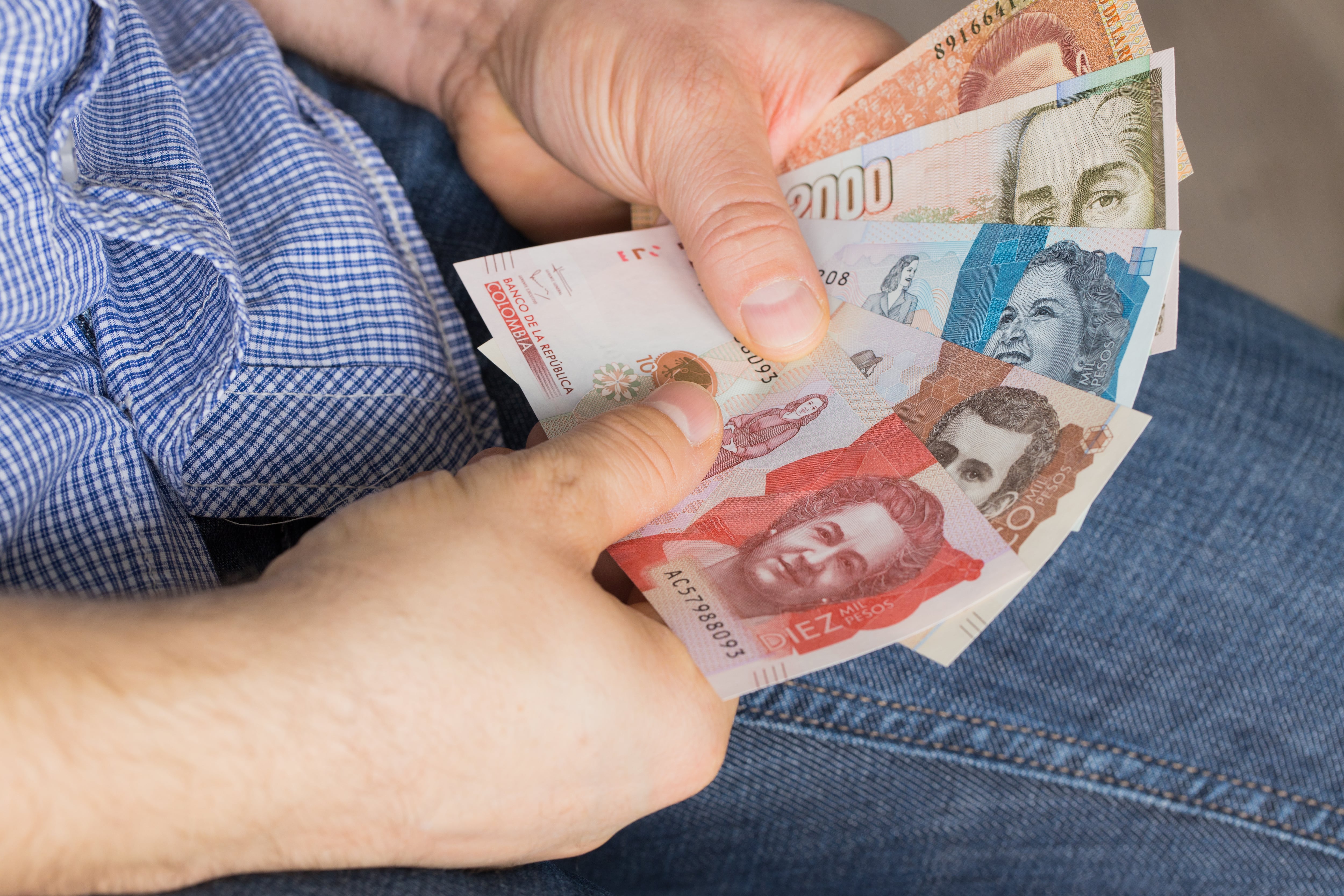 A man holding a bundle of money in his hands, various Colombian pesos