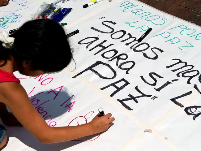 A girl writes on a placard messages alluding to peace on April 9, 2013, in Cali, Valle del Cauca department, Colombia, during a national march in support of the peace process ongoing in Havana between the Revolutionary Armed Forces of Colombia (FARC) guerrillas and the Colombian government . AFP PHOTO/Luis ROBAYO (Photo credit should read LUIS ROBAYO/AFP via Getty Images)
