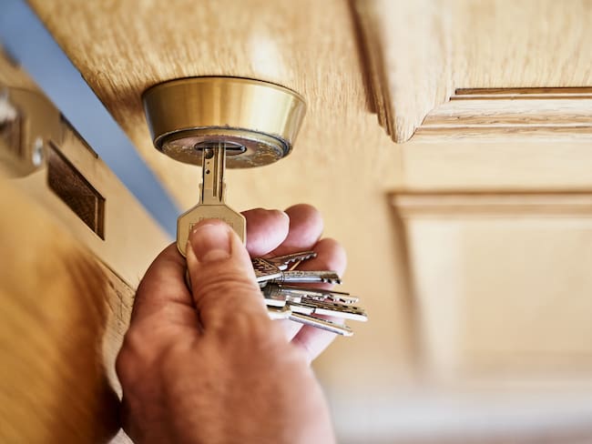 above view of caucasian person arriving close home holding a key opening a wooden door and taking out the key from the lock. The locksmith is old and rusty. Horizontal photogtaphy.
