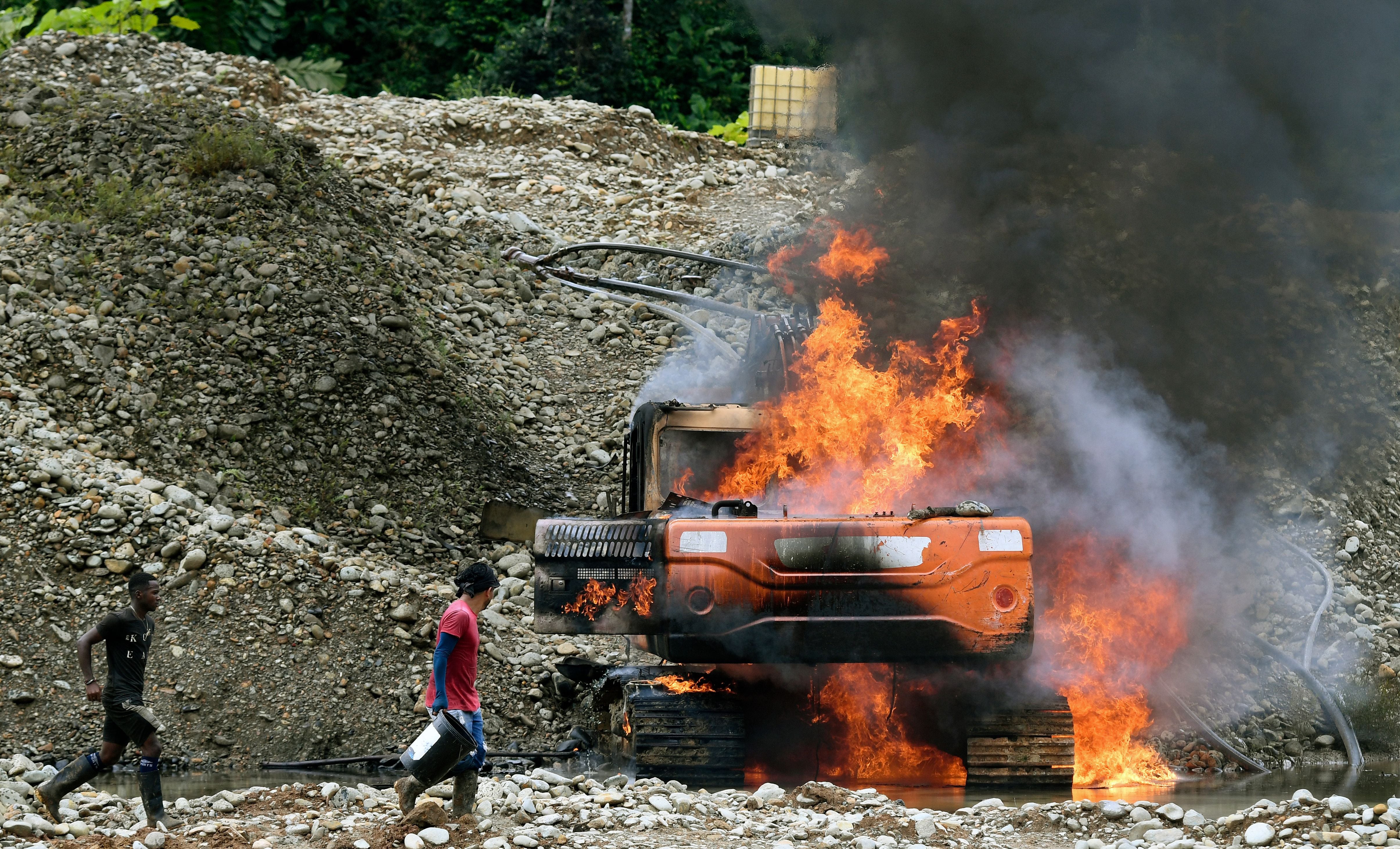 Los lugareños intentan apagar el fuego de la maquinaria pesada, destruida por las fuerzas armadas durante una operación en un lugar de minería ilegal de oro en Triángulo de Telembí, Colombia, el 25 de enero de 2023. (Daniel Muñoz/AFP vía Getty Images)
