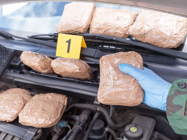 Police officer holding drug package discovered in engine compartment of a car