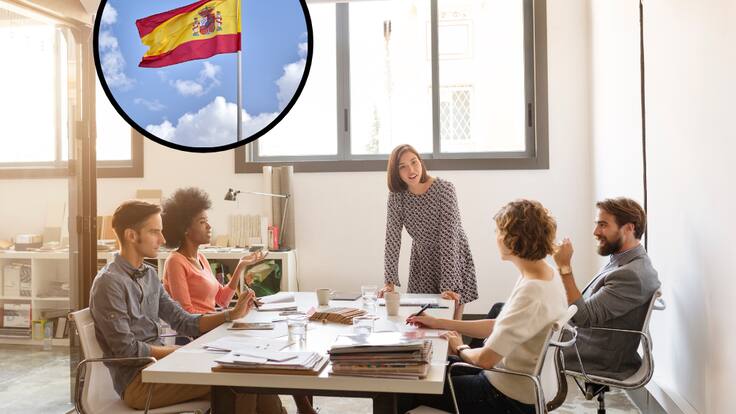 Colegas de trabajo teniendo una reunión y de fondo una bandera de España (Fotos vía Getty Images)