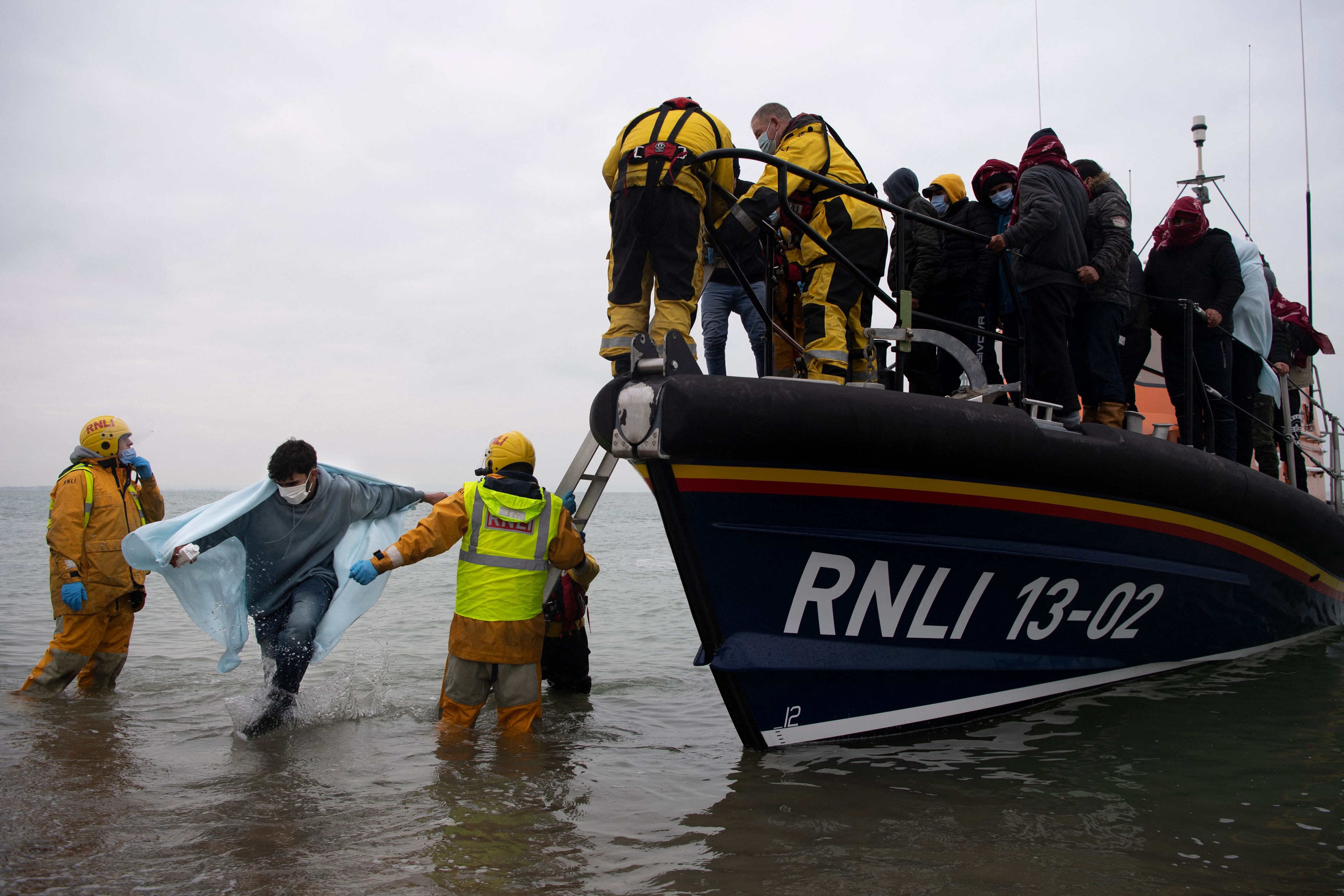 TOPSHOT - Migrants are helped ashore from a RNLI (Royal National Lifeboat Institution) lifeboat at a beach in Dungeness, on the south-east coast of England, on November 24, 2021, after being rescued while crossing the English Channel. - The past three years have seen a significant rise in attempted Channel crossings by migrants, despite warnings of the dangers in the busy shipping lane between northern France and southern England, which is subject to strong currents and low temperatures. (Photo by Ben STANSALL / AFP) (Photo by BEN STANSALL/AFP via Getty Images)