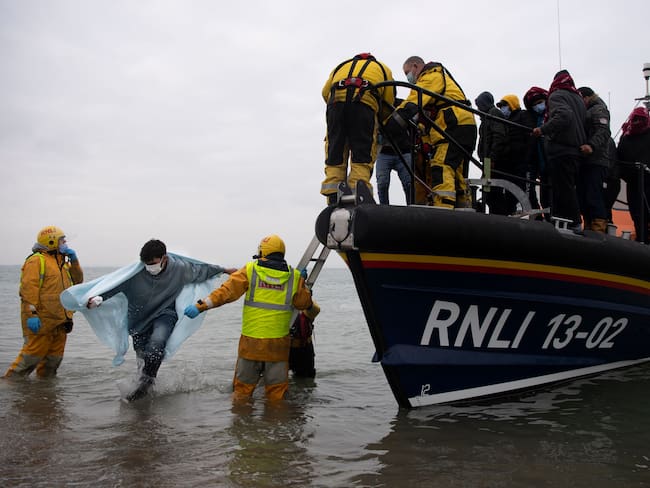 TOPSHOT - Migrants are helped ashore from a RNLI (Royal National Lifeboat Institution) lifeboat at a beach in Dungeness, on the south-east coast of England, on November 24, 2021, after being rescued while crossing the English Channel. - The past three years have seen a significant rise in attempted Channel crossings by migrants, despite warnings of the dangers in the busy shipping lane between northern France and southern England, which is subject to strong currents and low temperatures. (Photo by Ben STANSALL / AFP) (Photo by BEN STANSALL/AFP via Getty Images)