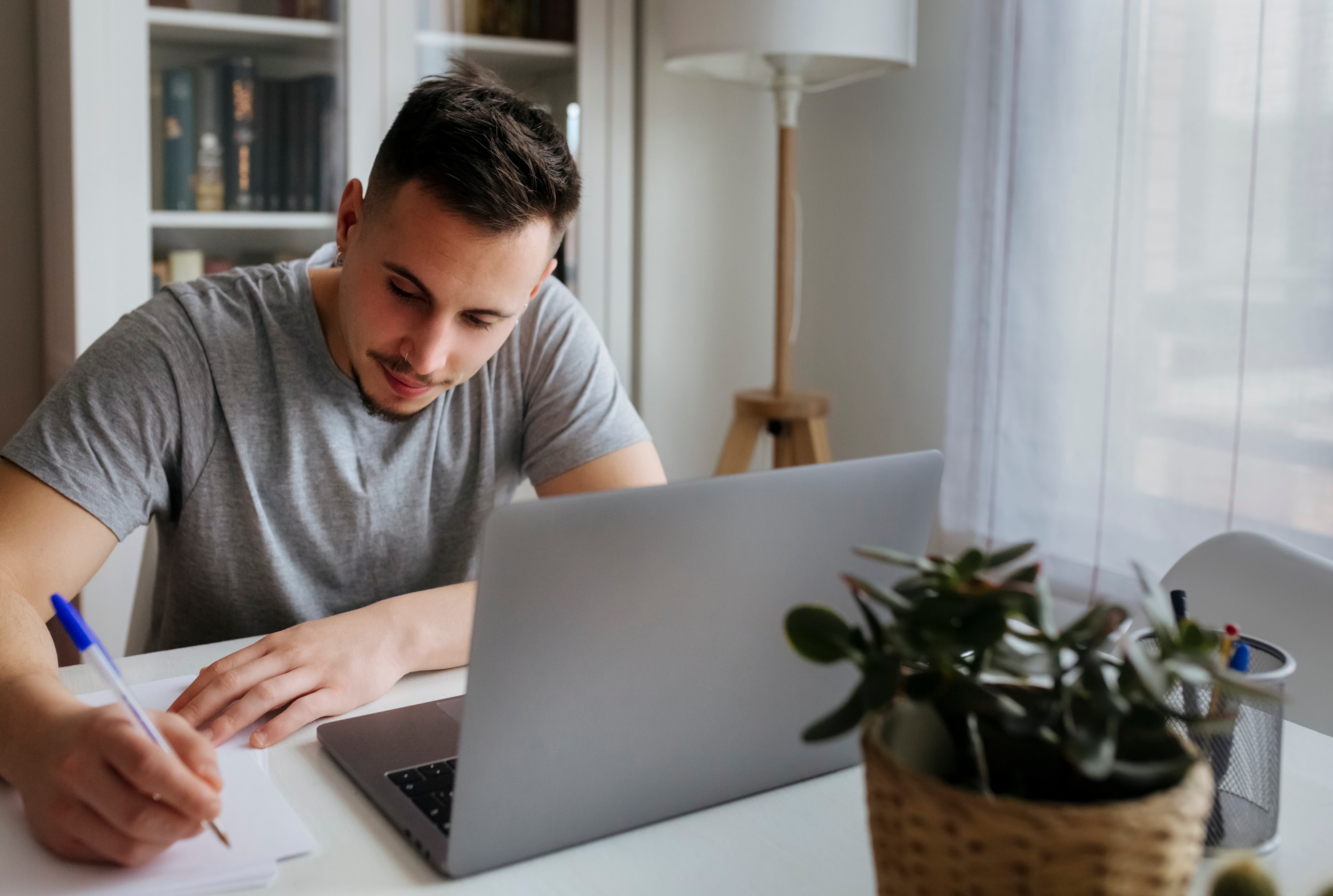 Hombre escribiendo en papel mientras está sentado con un computador portátil en su casa / Foto: GettyImages