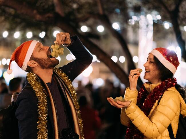 Happy couple celebrating New Year outside at night and eating grapes