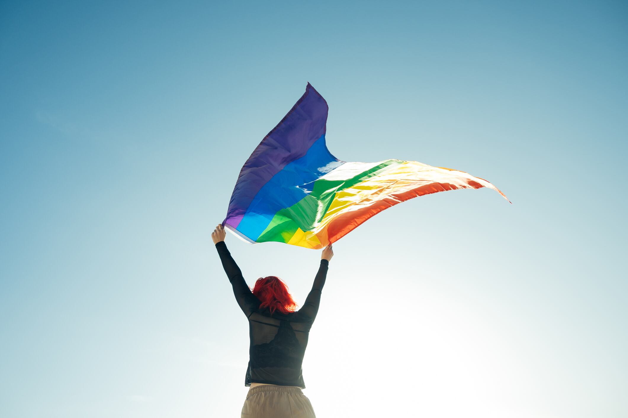 Woman holding the Gay Rainbow Flag on blue sky background. Happiness, freedom and love concept for same sex couples. (Woman holding the Gay Rainbow Flag on blue sky background. Happiness, freedom and love concept for same sex couples., ASCII, 117 comp