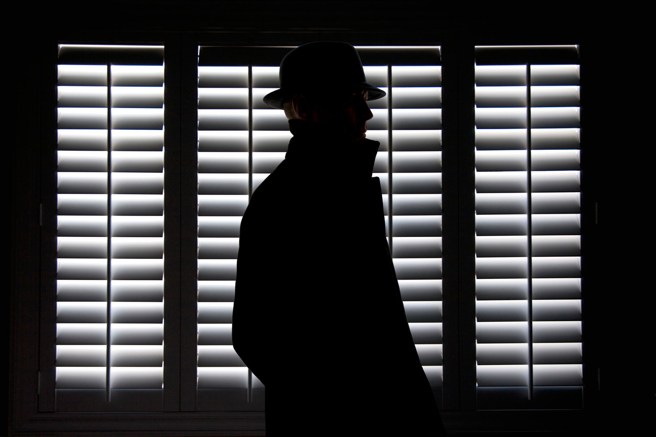 Silhouette of a man in hat against screen window.