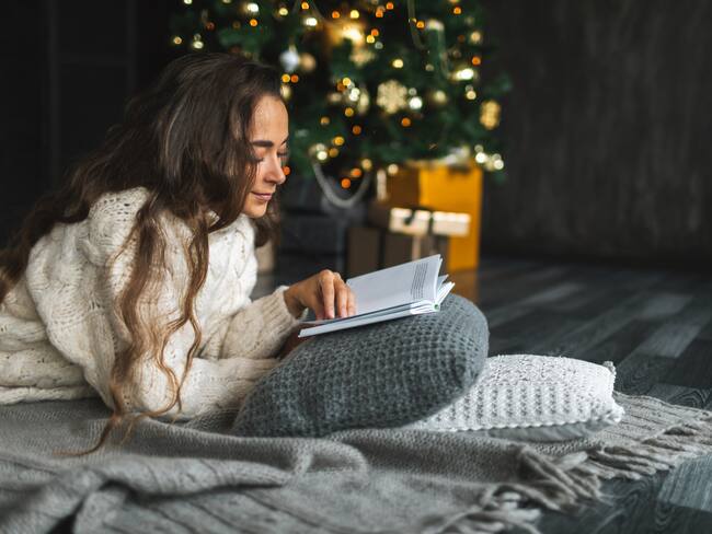 Beautiful long hair woman is reading book in front of Christmas tree. Christmas and holidays concept.