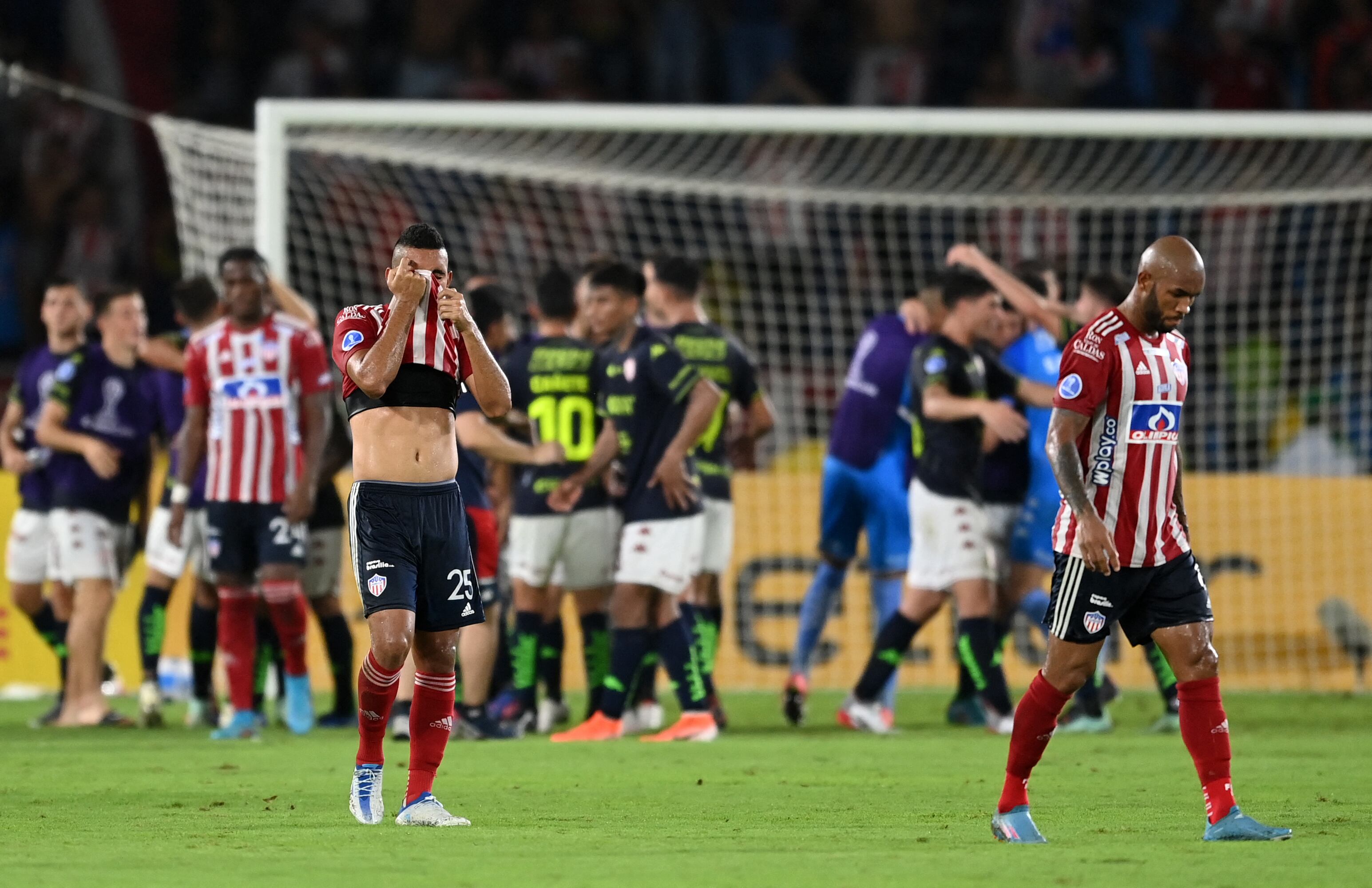 Colombia's Junior Carlos Esparragoza (L) reacts as Argentina's Union de Santa Fe players (background) celebrate at the end of the Copa Sudamericana group stage football match, at the Roberto Melendez Metropolitan stadium, in Barranquilla, Colombia, on May 26, 2022. (Photo by YURI CORTEZ / AFP)