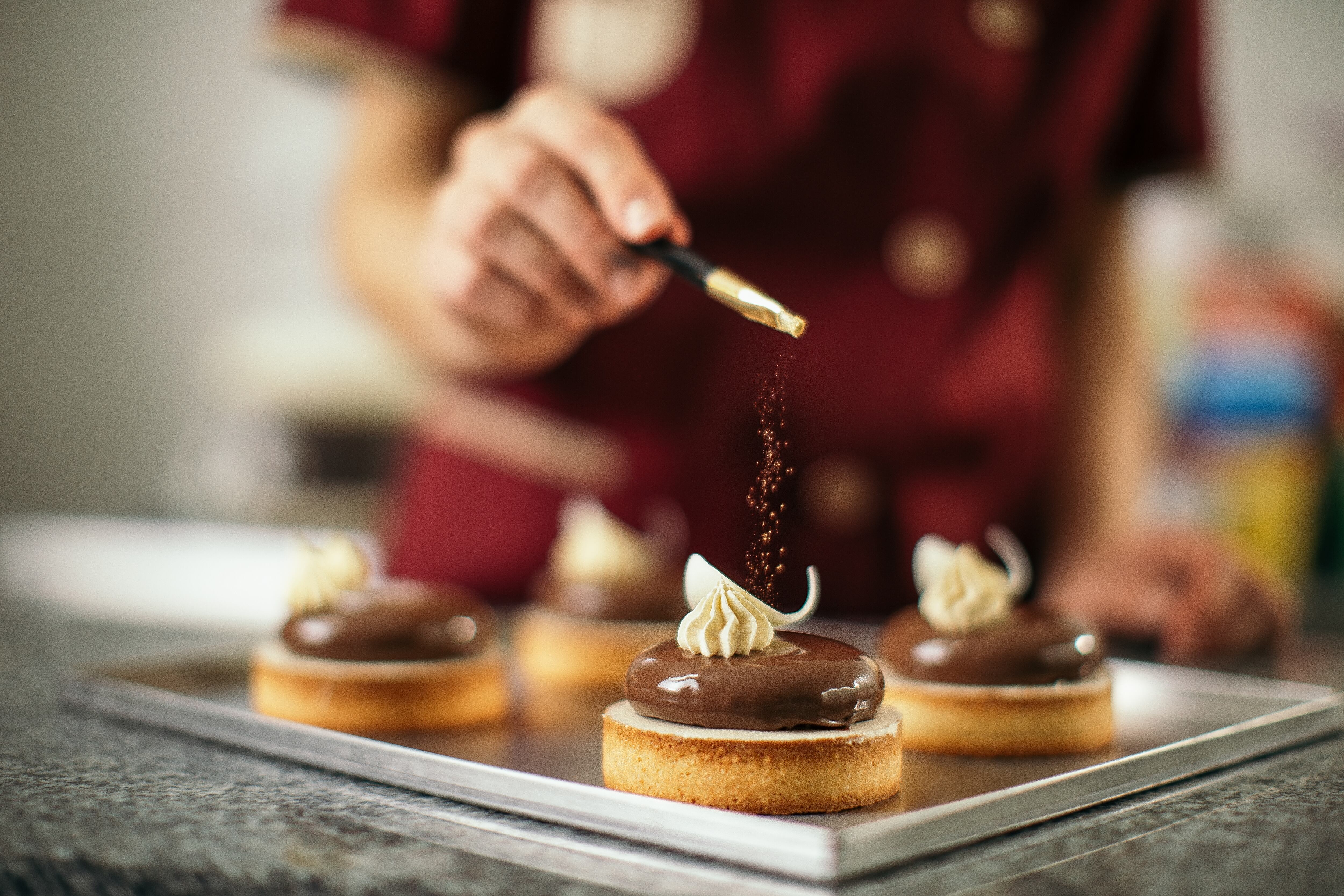 Mid adult woman decorating chocolate cookies with sweet powder on top. She works in sweet food manufacture, small business company