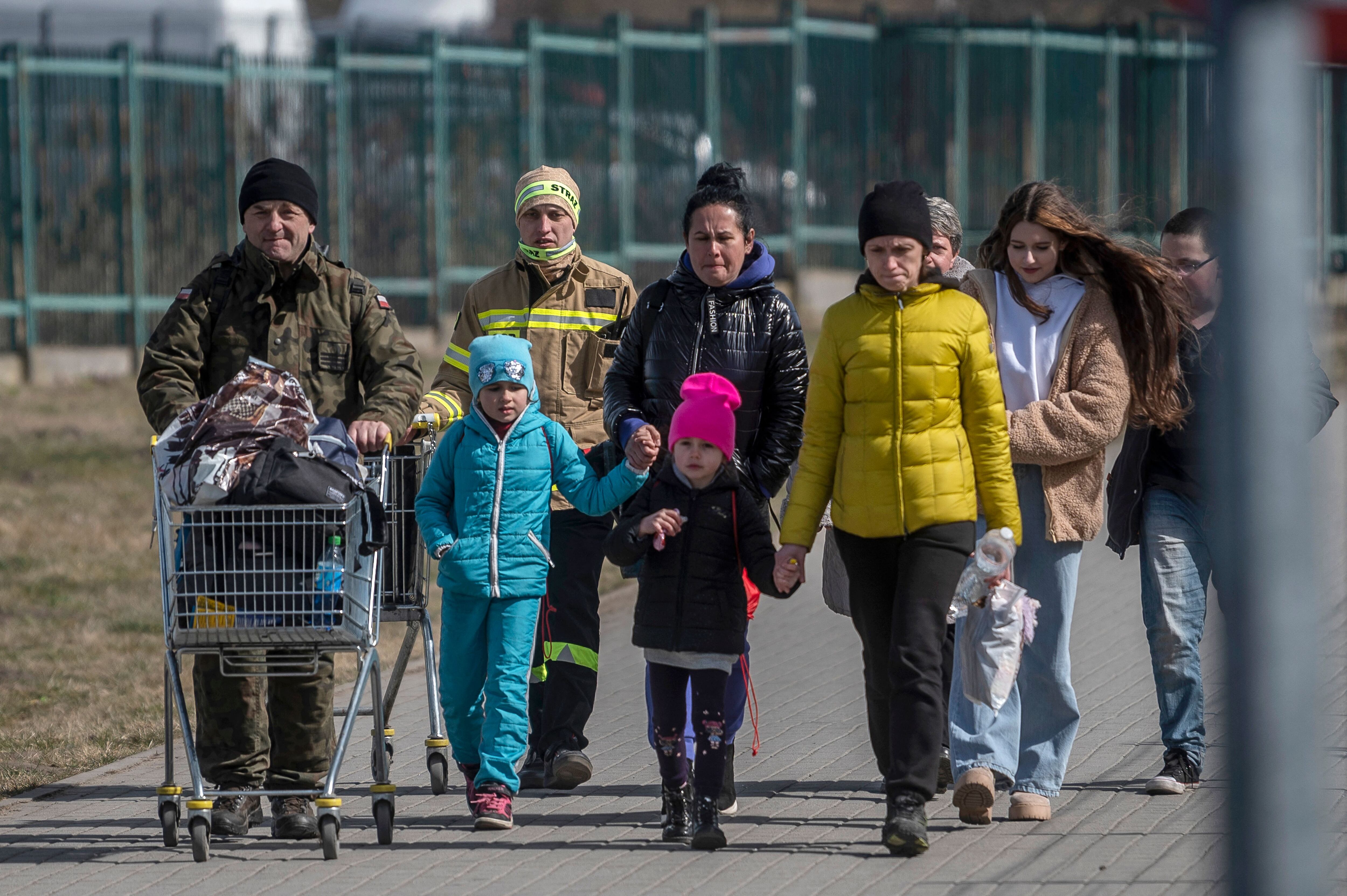 A Polish serviceman (L) helps Ukrainian refugees to cross the Ukrainian border with Poland at the Medyka border crossing, southeastern Poland, on March 27, 2022, following Russia's invasion of Ukraine about one month ago. (Photo by Angelos Tzortzinis / AFP) (Photo by ANGELOS TZORTZINIS/AFP via Getty Images)