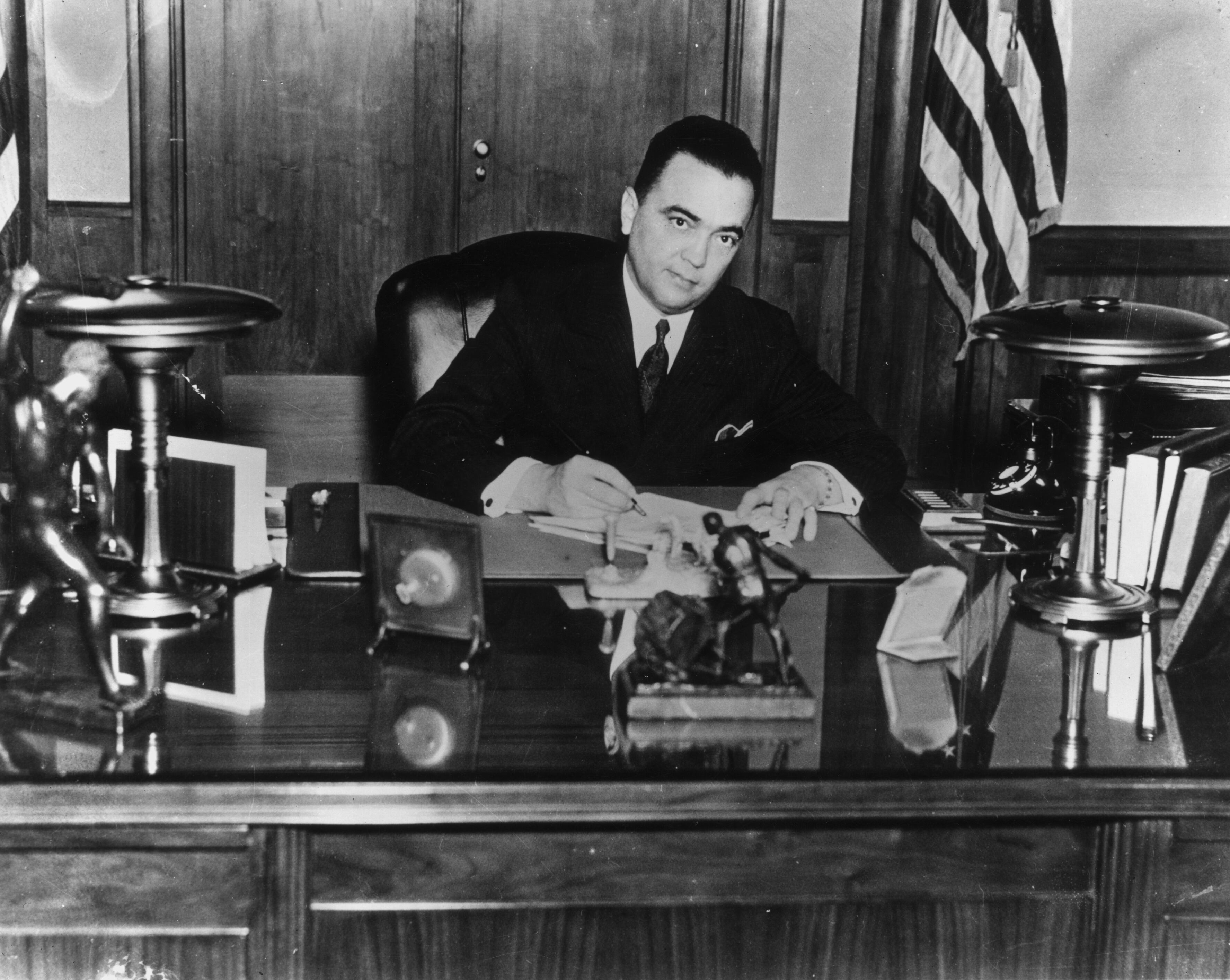 circa 1935: Portrait of FBI director J. Edgar Hoover (1895 - 1972) sitting at a desk while signing a document. (Photo by American Stock/Getty Images)