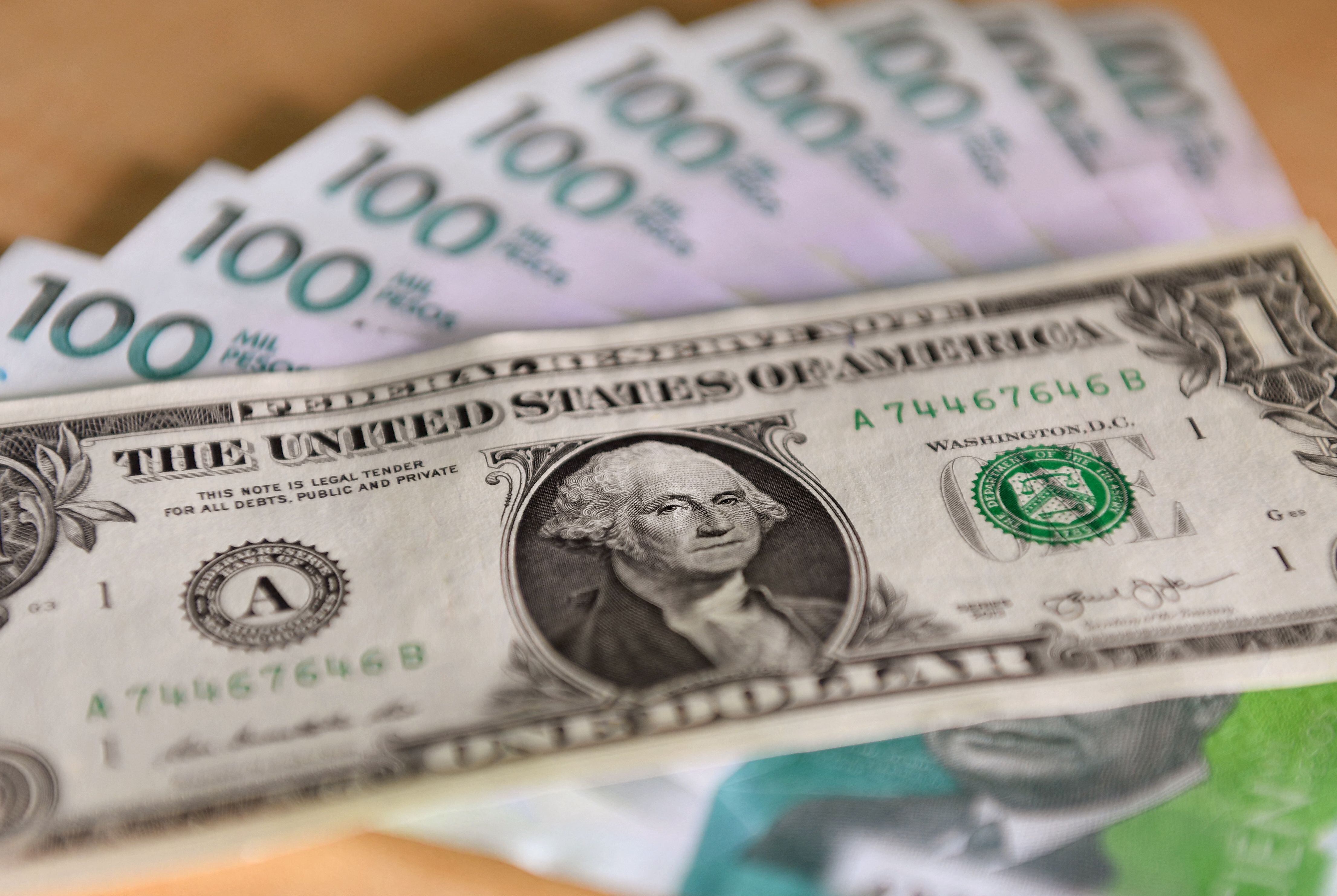 Imagen de un billete de un dólar estadounidense sobre billetes colombianos de cien mil pesos tomada en Bogotá el 24 de octubre de 2022. (Daniel Muñoz/AFP vía Getty Images)