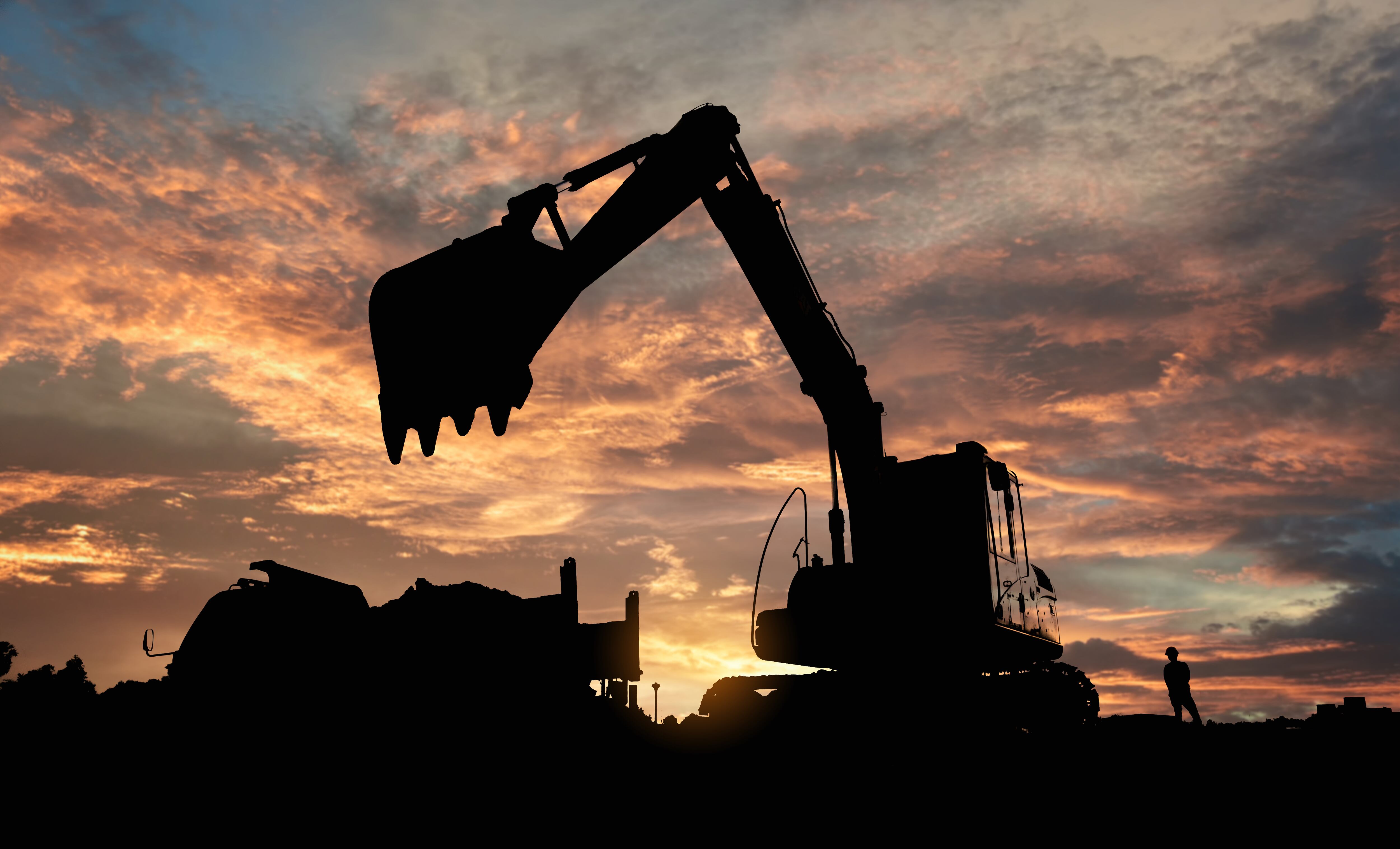 Various pieces of construction equipment are sihouetted by the sunset