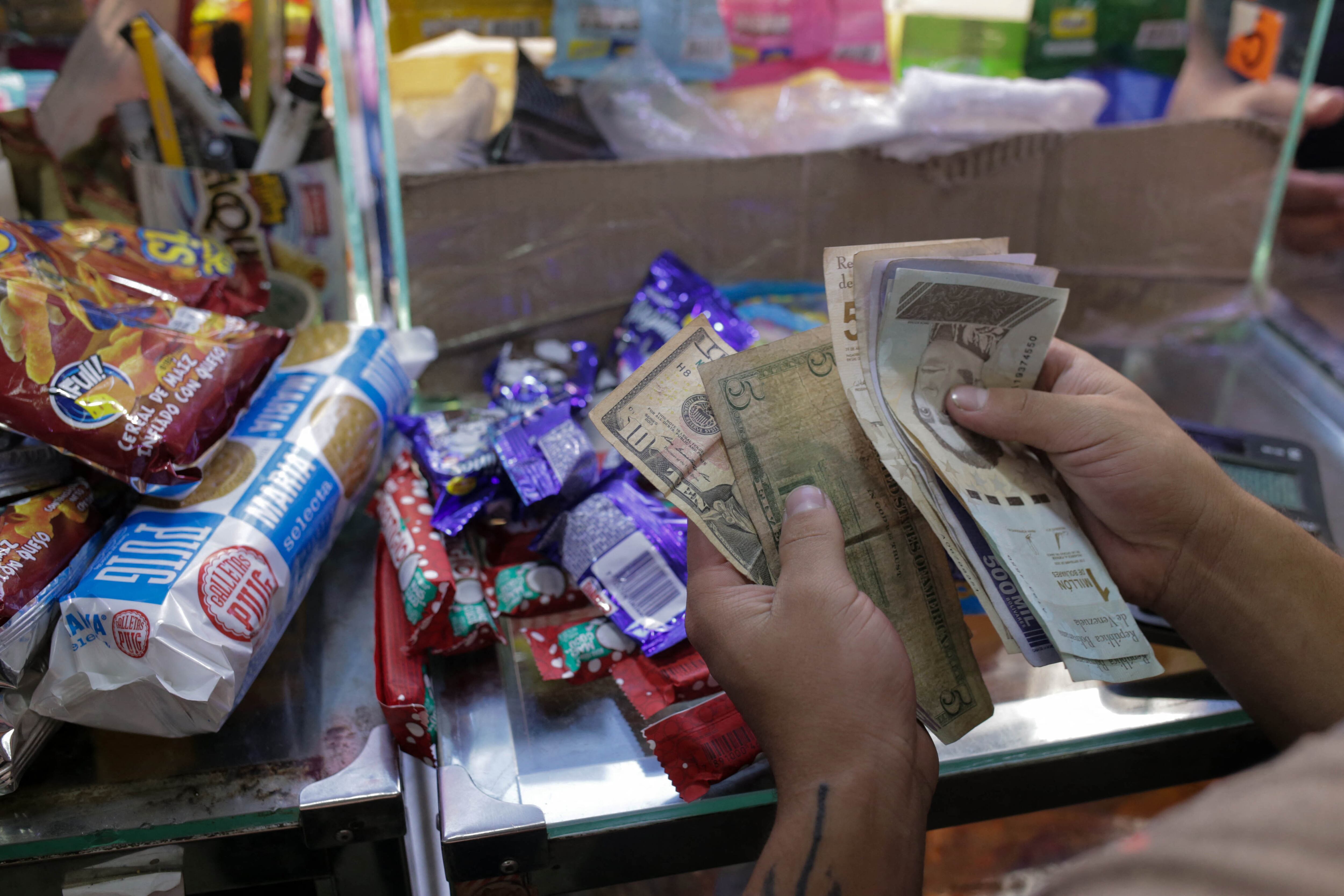 A vendor counts Venezuelan Bolivars and US dollar notes at a grocery store, in Caracas, on January 13, 2022. - Despite the fact that the country is emerging -after four years- from an uncontrolled era of inflation, Venezuelan people consider there is not a change in the prices increase. (Photo by CRISTIAN HERNANDEZ / AFP) (Photo by CRISTIAN HERNANDEZ/AFP via Getty Images)
