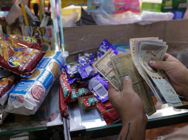 A vendor counts Venezuelan Bolivars and US dollar notes at a grocery store, in Caracas, on January 13, 2022. - Despite the fact that the country is emerging -after four years- from an uncontrolled era of inflation, Venezuelan people consider there is not a change in the prices increase. (Photo by CRISTIAN HERNANDEZ / AFP) (Photo by CRISTIAN HERNANDEZ/AFP via Getty Images)