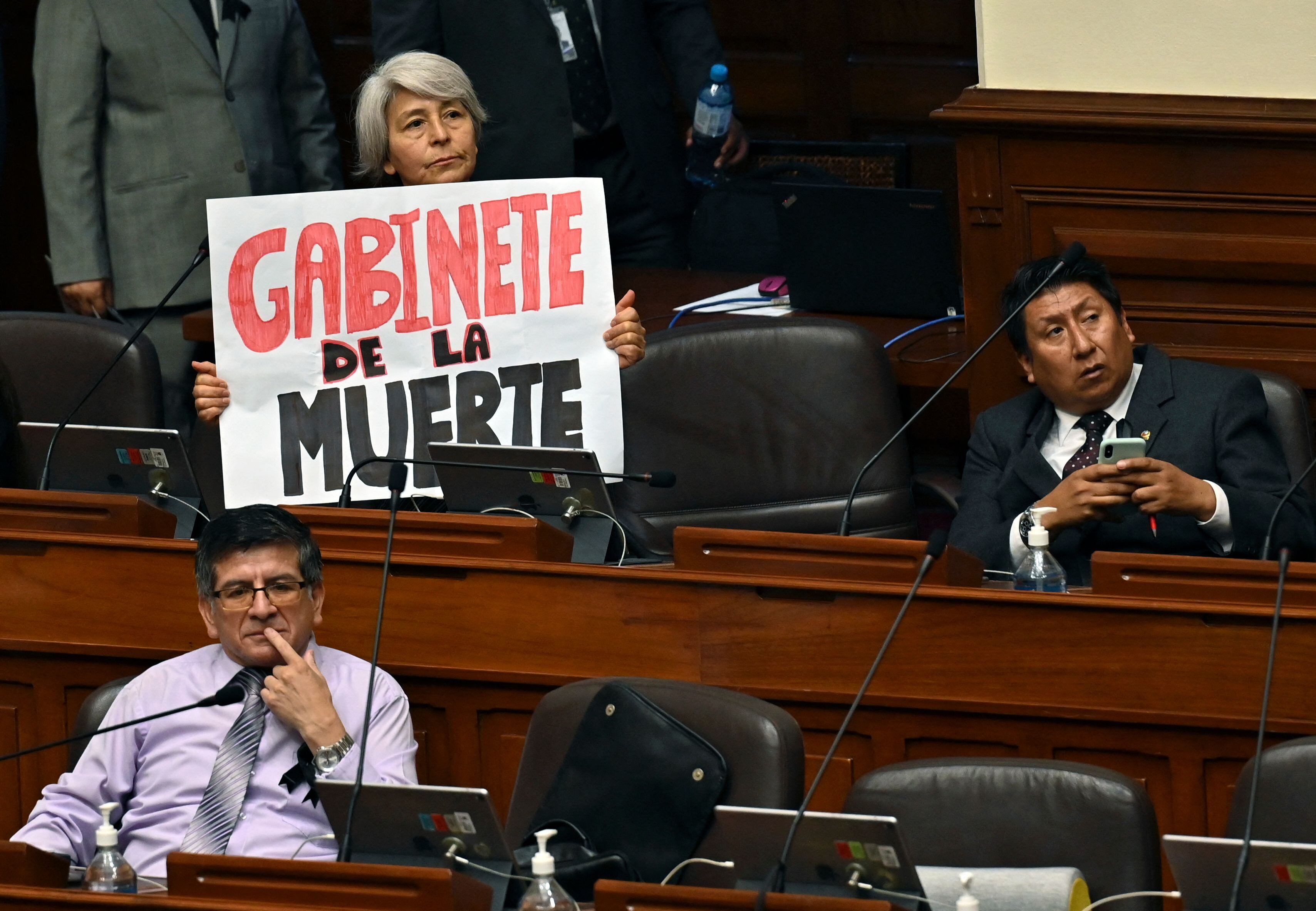 La diputada peruana Margot Agüero, del partido de izquierda Perú Libre, sostiene un cartel que dice "Gabinete de la muerte" durante la sesión plenaria del Congreso, en Lima, el 10 de enero de 2023. -Foto de CRIS BOURONCLE/POOL/AFP vía Getty Images.