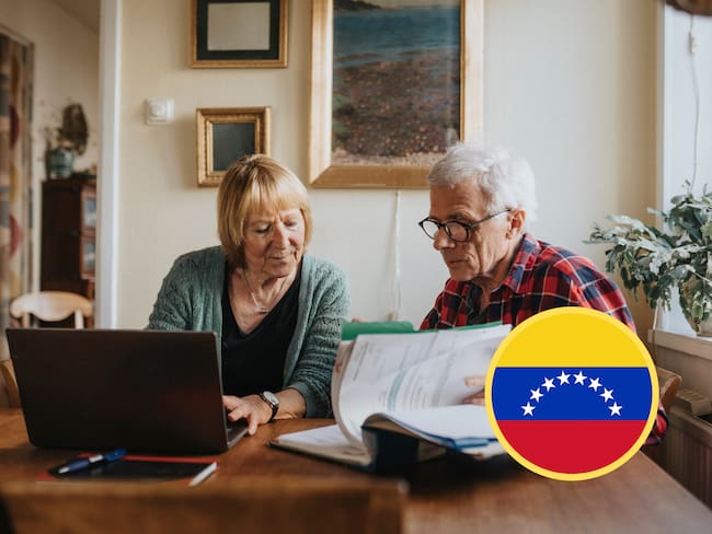 Pareja de adultos mayores usando computador, junto a bandera de Venezuela (GettyImages)