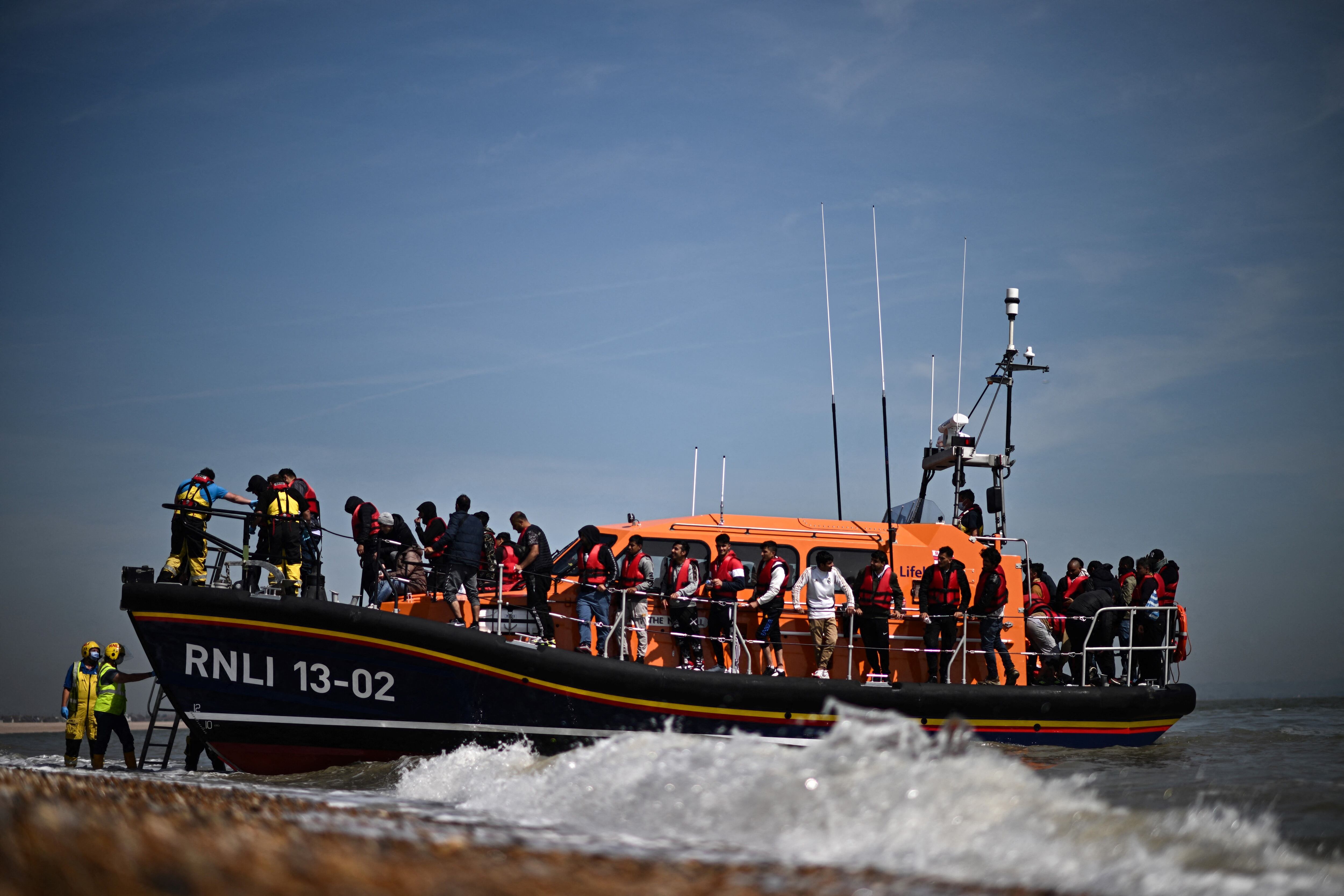 Migrantes en el mar que intentaban cruzar el Canal de la Mancha son ayudados a desembarcar desde un bote salvavidas de la Royal National Lifeboat Institution (RNLI) en Dungeness, en la costa sureste de Inglaterra, el 15 de junio de 2022.(Photo by Ben Stansall / AFP) (Photo by BEN STANSALL/AFP via Getty Images)