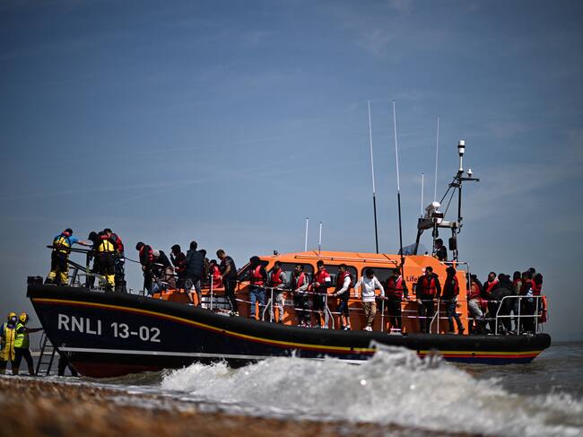 Migrantes en el mar que intentaban cruzar el Canal de la Mancha son ayudados a desembarcar desde un bote salvavidas de la Royal National Lifeboat Institution (RNLI) en Dungeness, en la costa sureste de Inglaterra, el 15 de junio de 2022.(Photo by Ben Stansall / AFP) (Photo by BEN STANSALL/AFP via Getty Images)