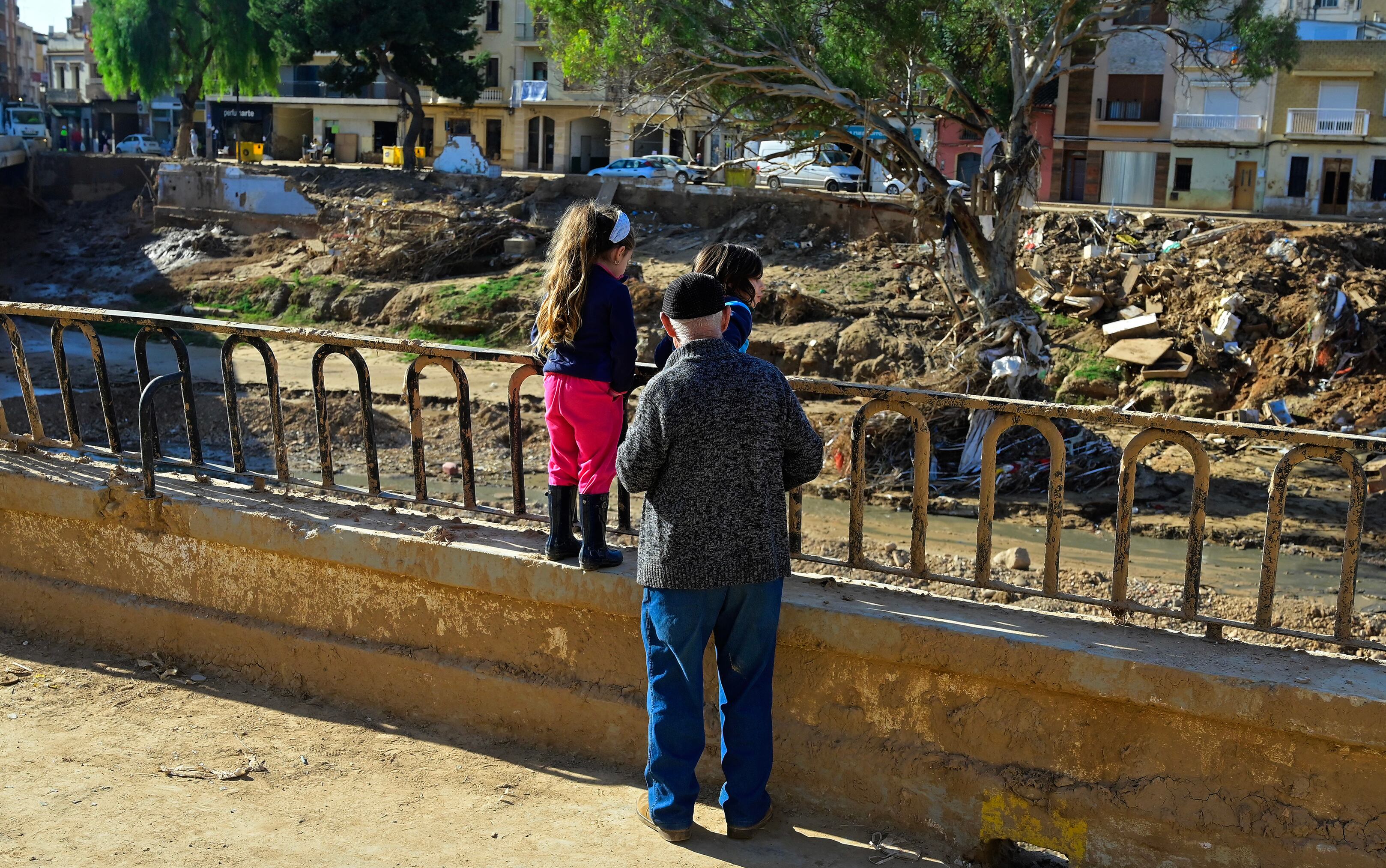 Un abuelo con sus dos nietas observan la destrucción en un barranco tras las inundaciones en Paiporta, cerca de Valencia, este de España, el 27 de noviembre de 2024. ( Jose Jordan / AFP)