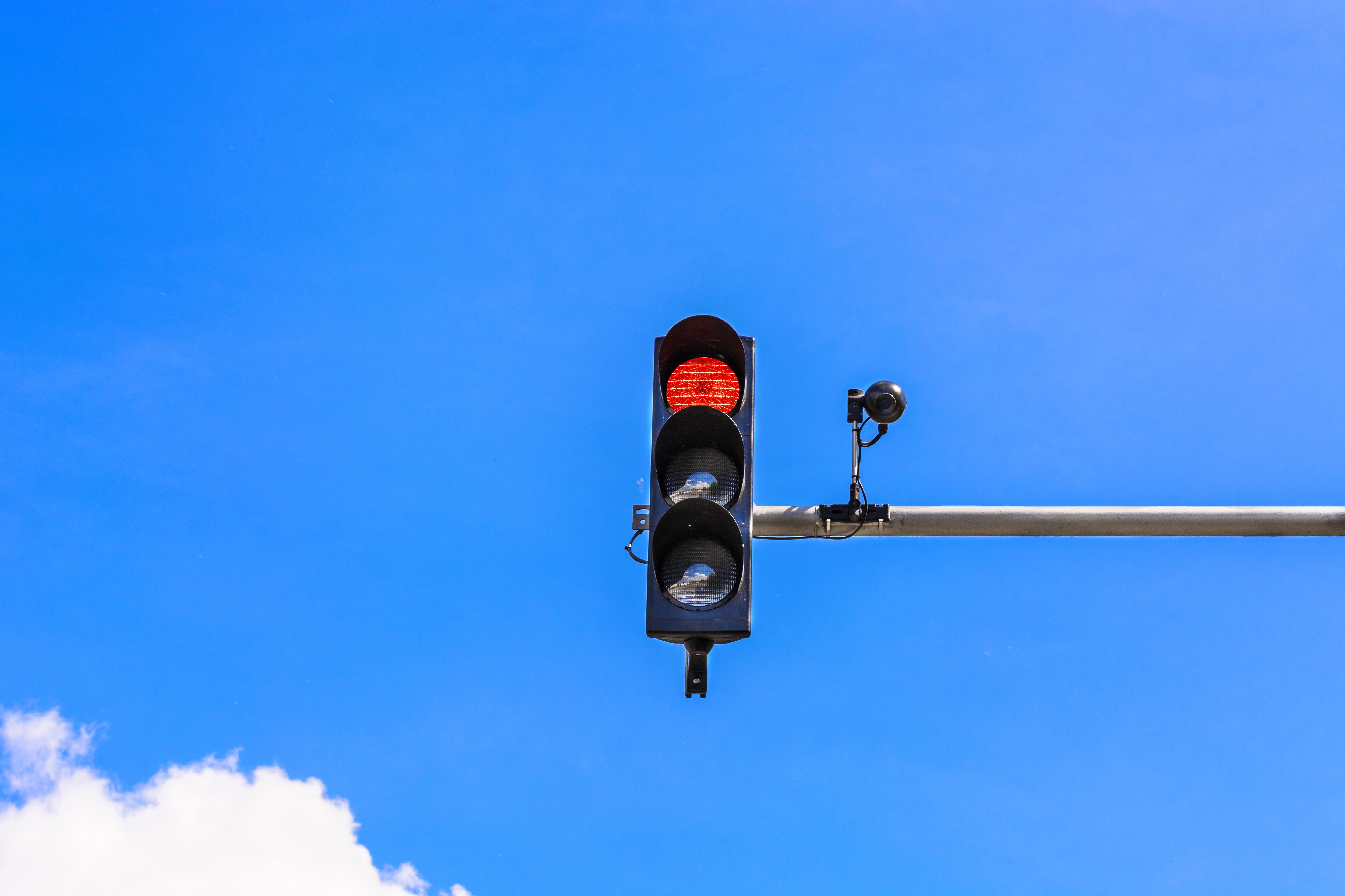 A traffic light and a surveillance camera on a pole mounted on the street.