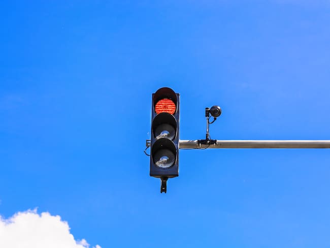 A traffic light and a surveillance camera on a pole mounted on the street.